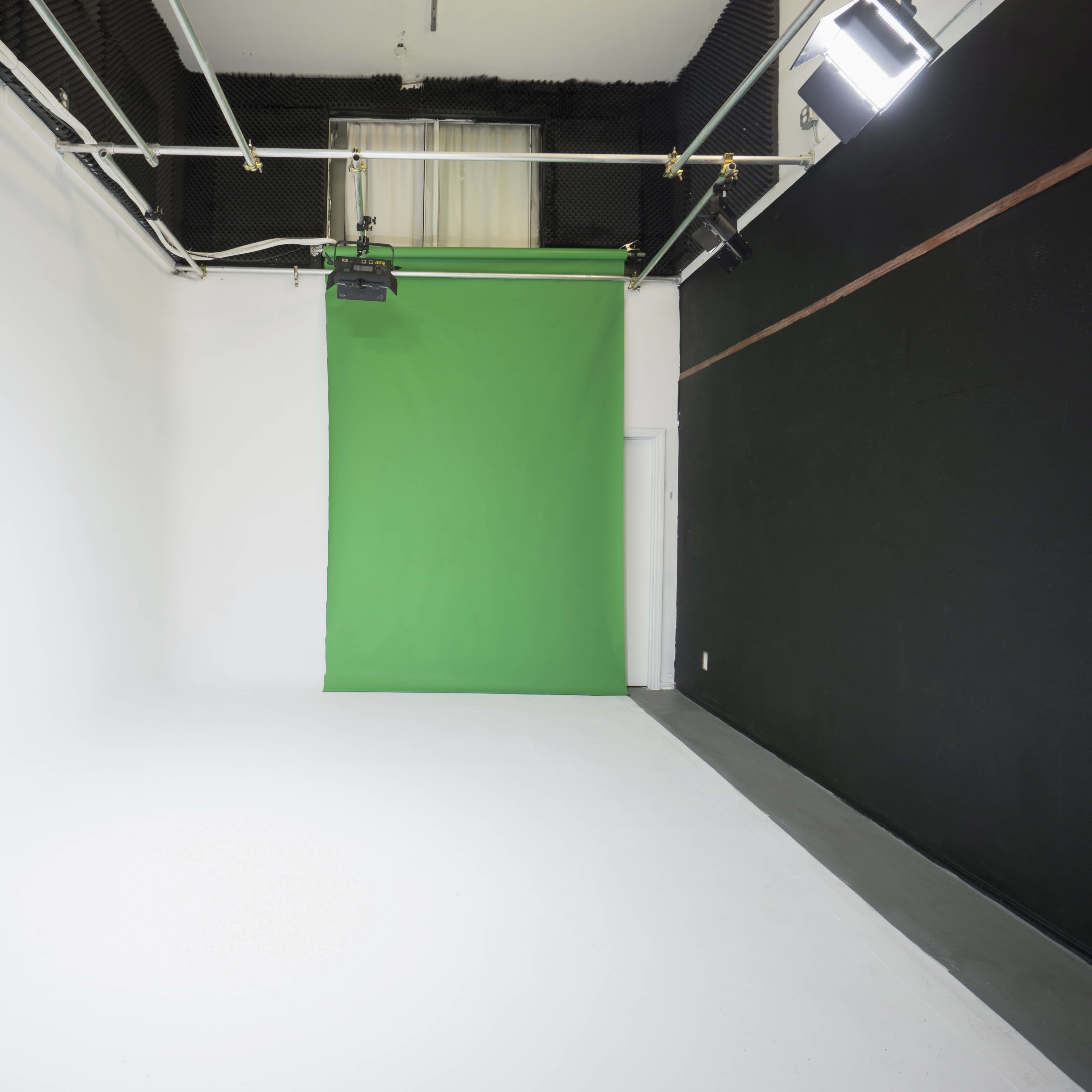 A photography studio with a green backdrop in the center and white walls on one side.