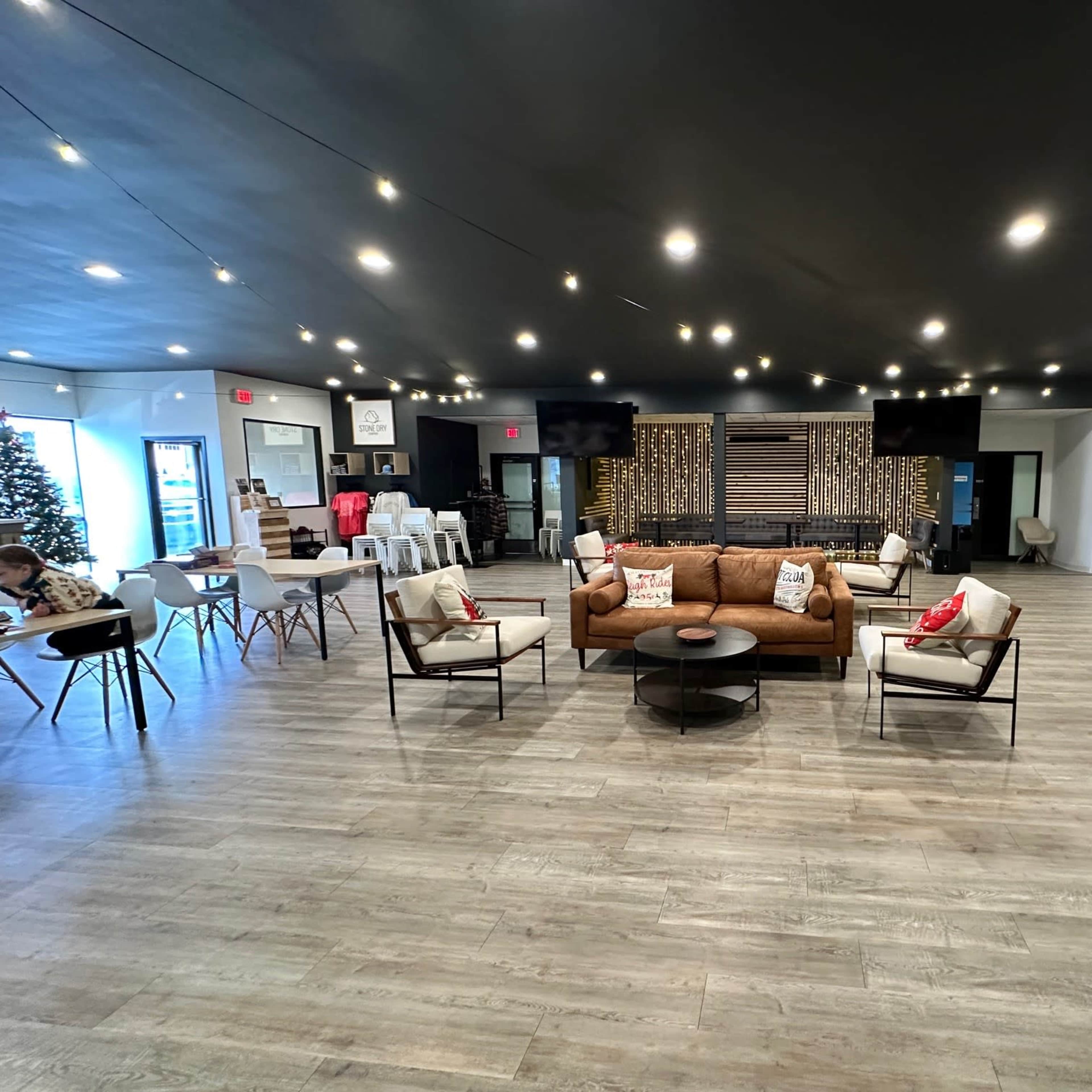 The interior of a modern event space features a brown sofa, white chairs, tables, and decorative lights.