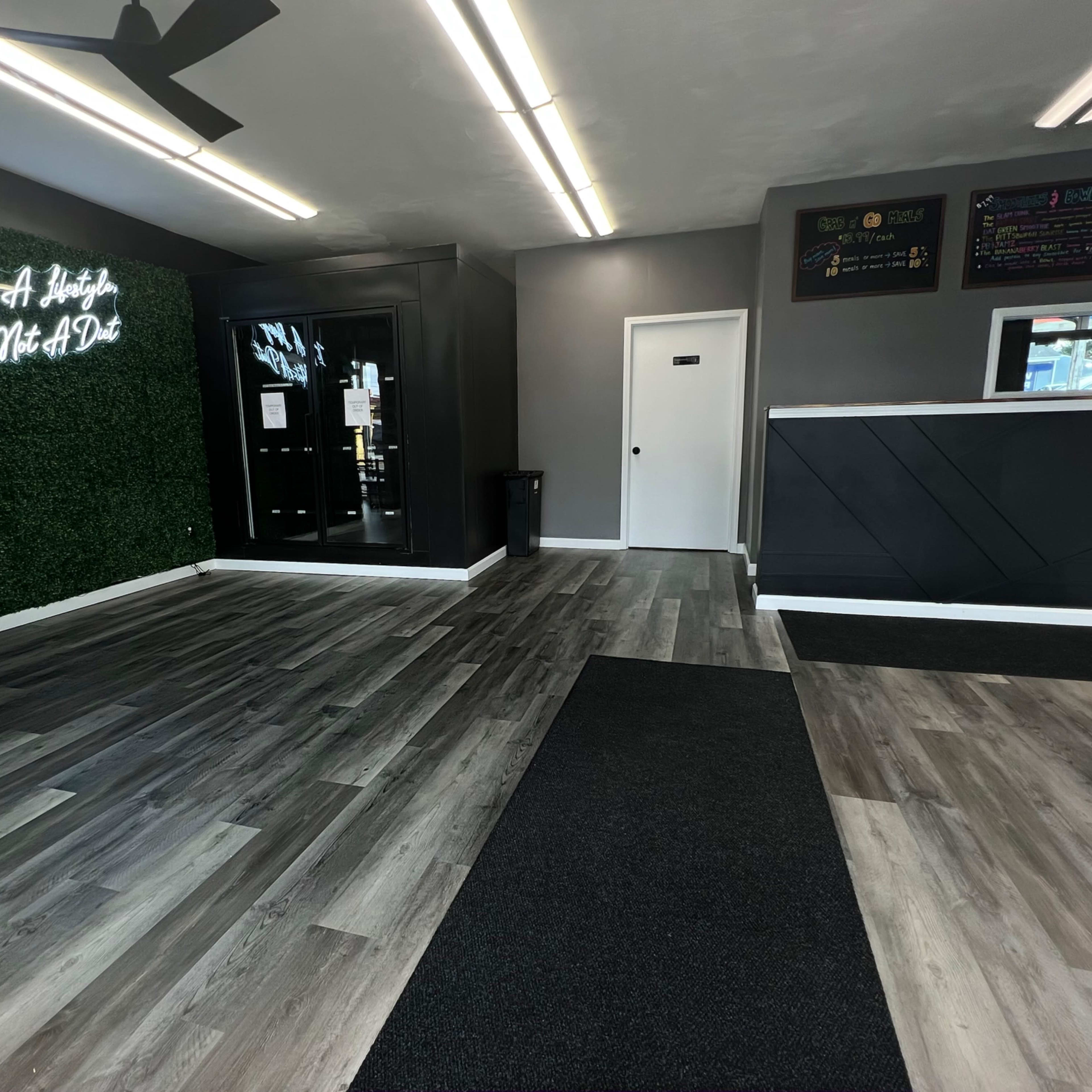 A spacious interior with a reception area featuring a dark counter, green accent wall with decorative lighting, and a large open floor.