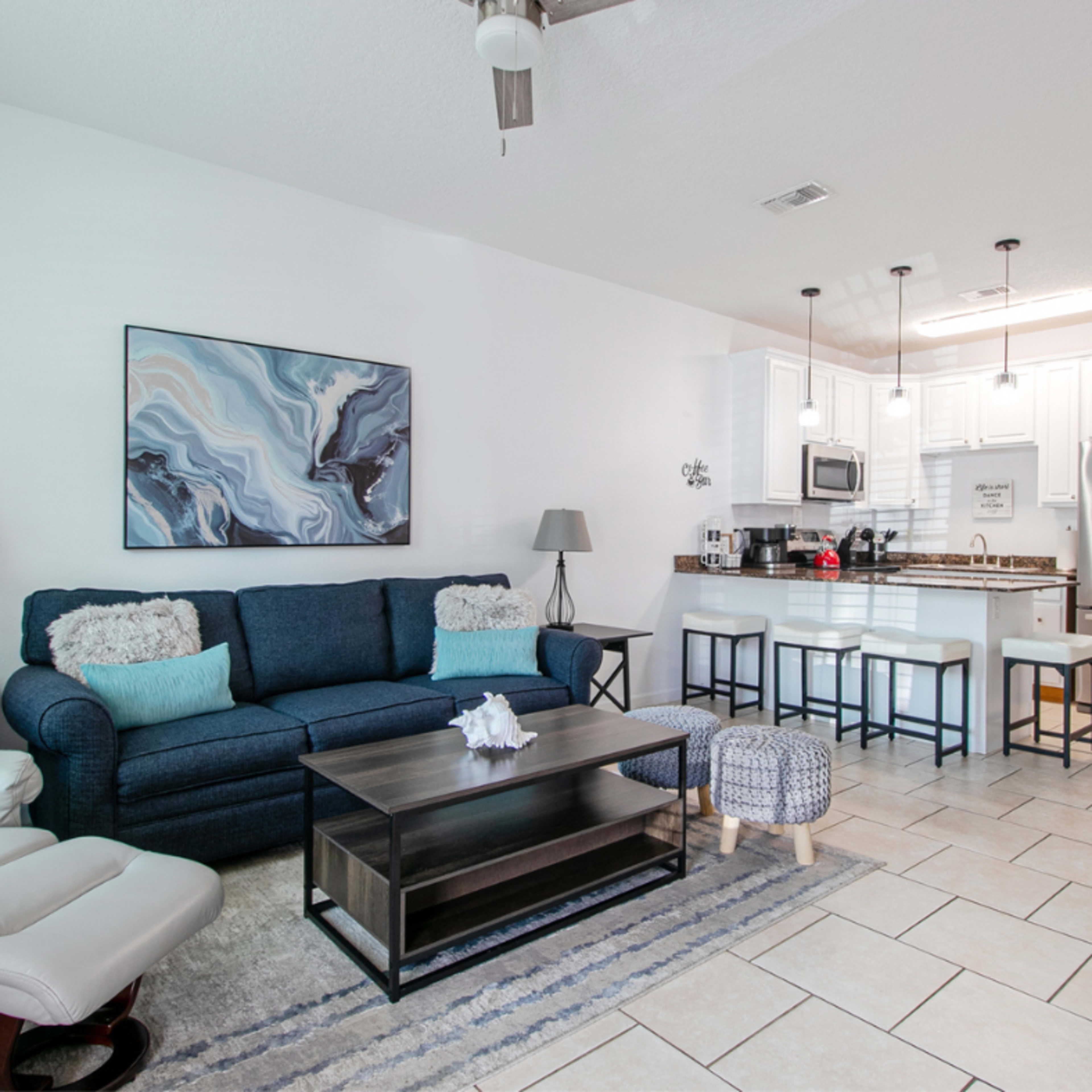 A modern living area with a blue sofa, a coffee table, and an open kitchen featuring white cabinets and stainless steel appliances.