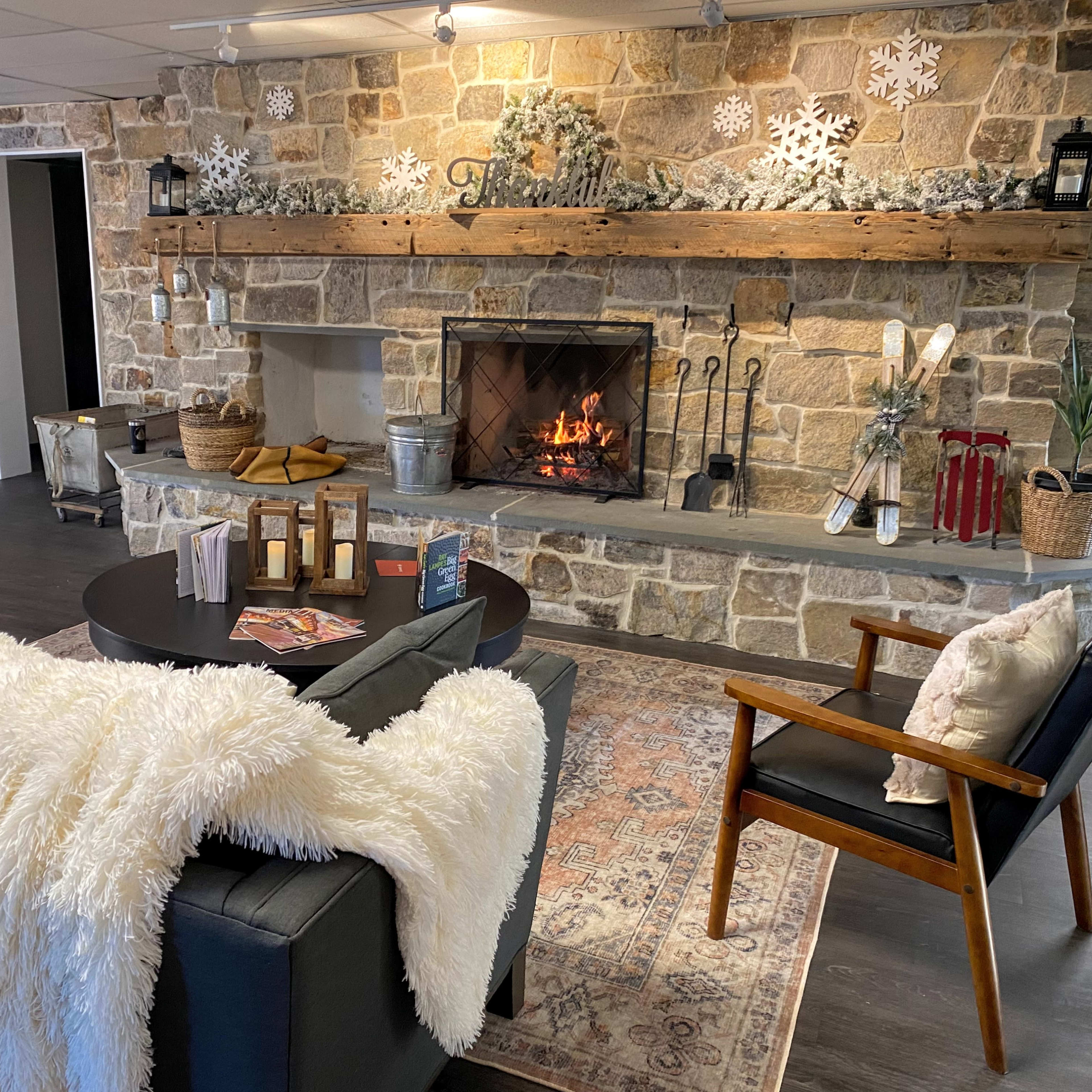 A cozy sitting area with a stone fireplace, wooden mantel, and a sofa draped with a white throw.
