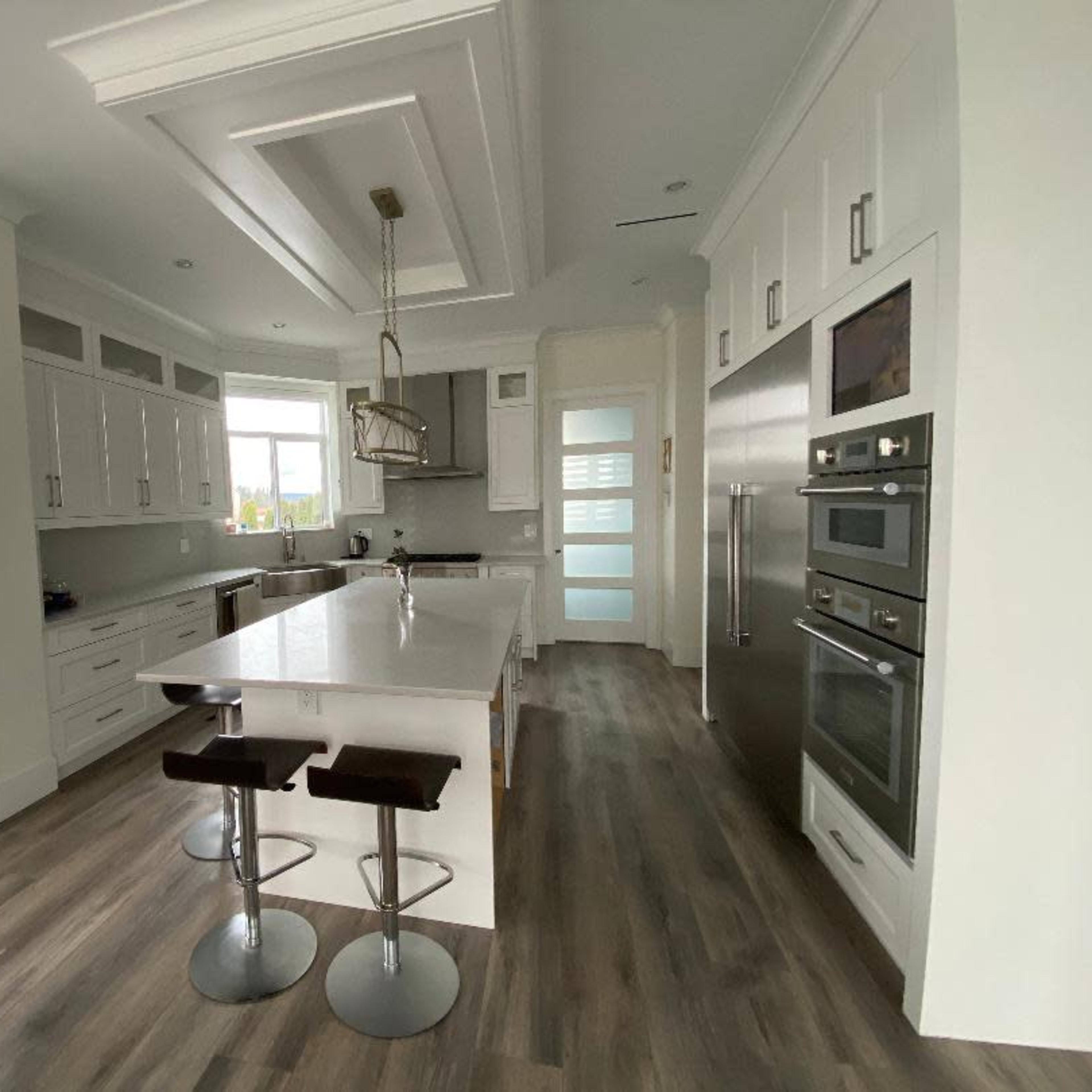 A modern kitchen features white cabinetry, a large island with bar stools, and stainless steel appliances.