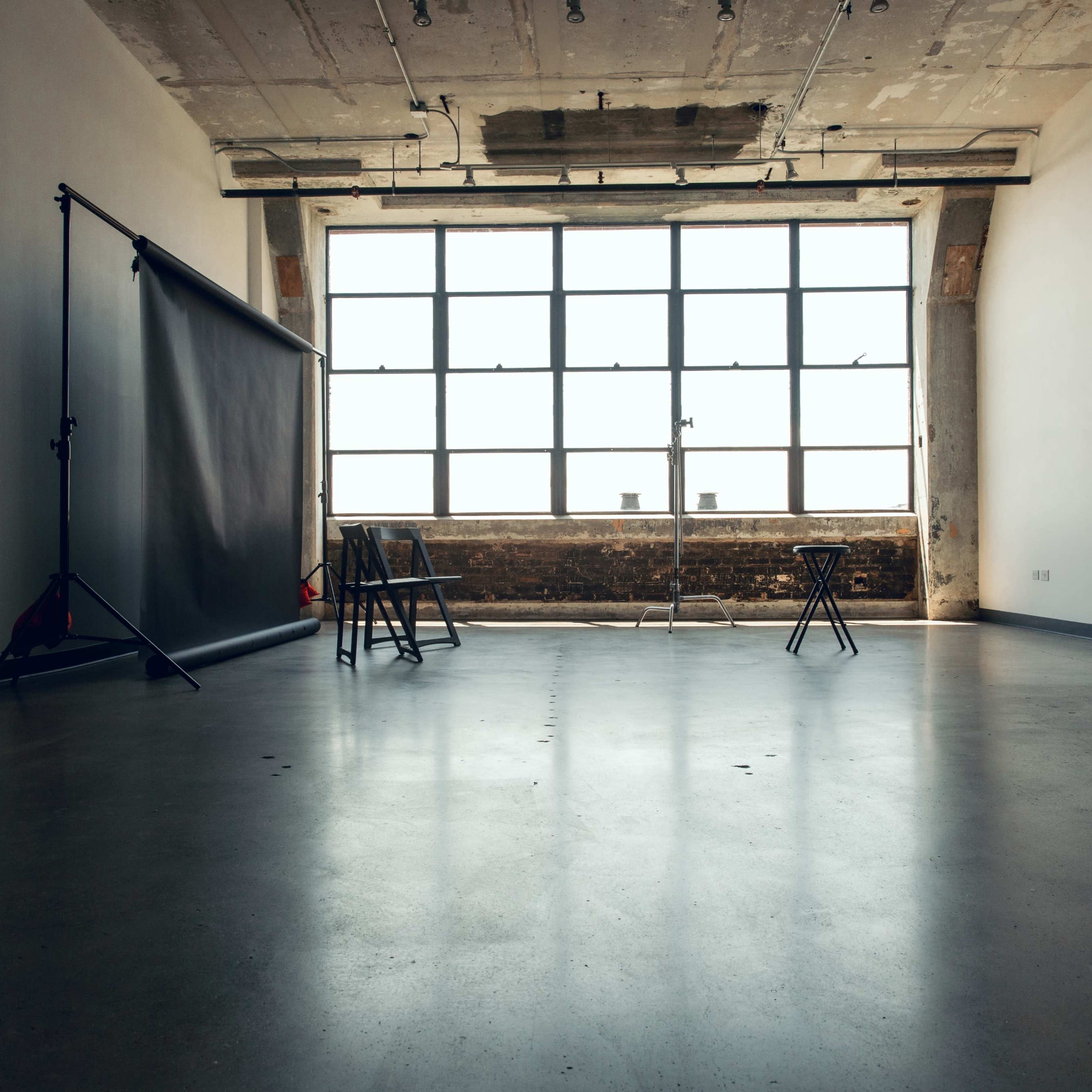 An empty room with a large window and a backdrop setup for photography.