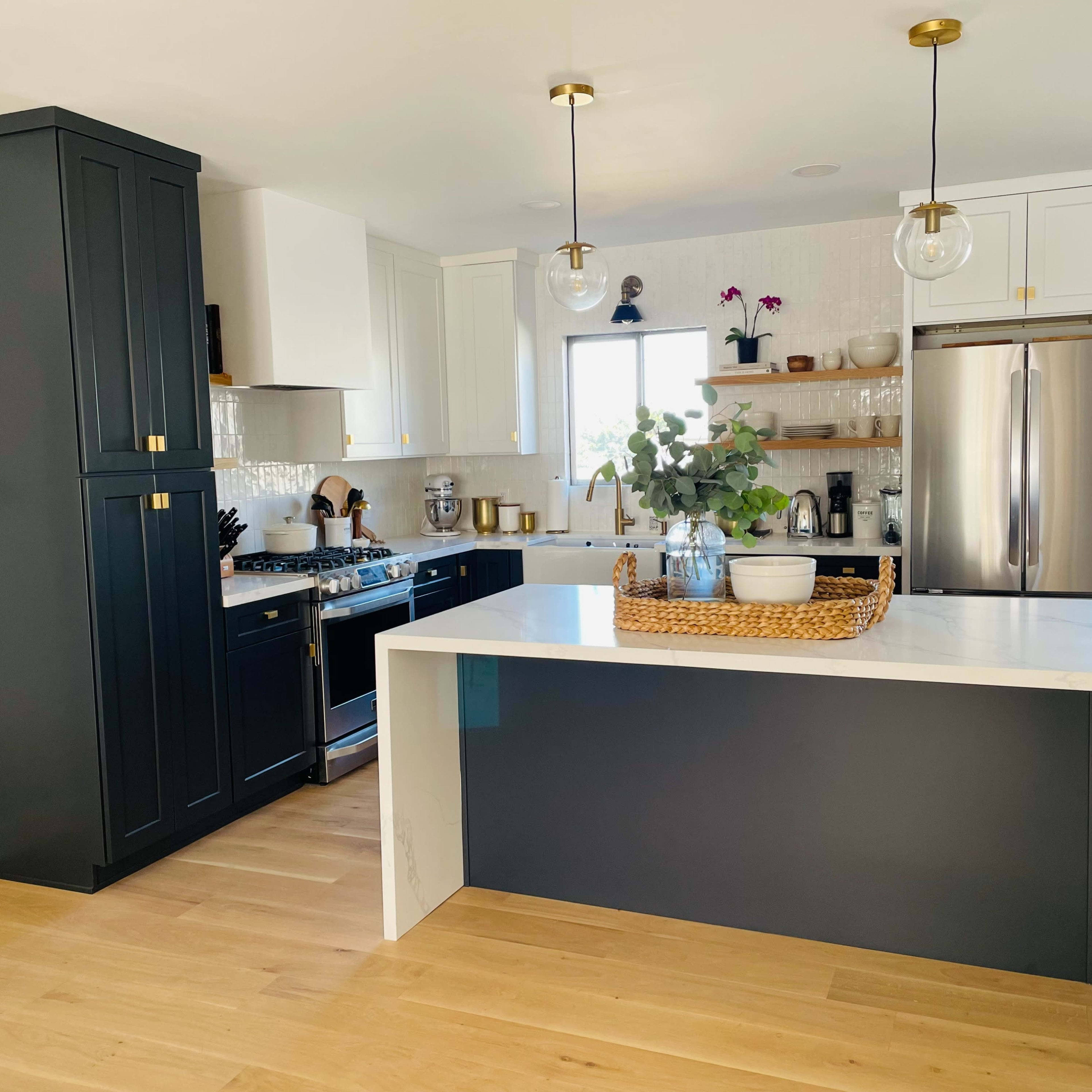 A modern kitchen features dark cabinetry, a bright island, stainless steel appliances, and natural wood flooring.