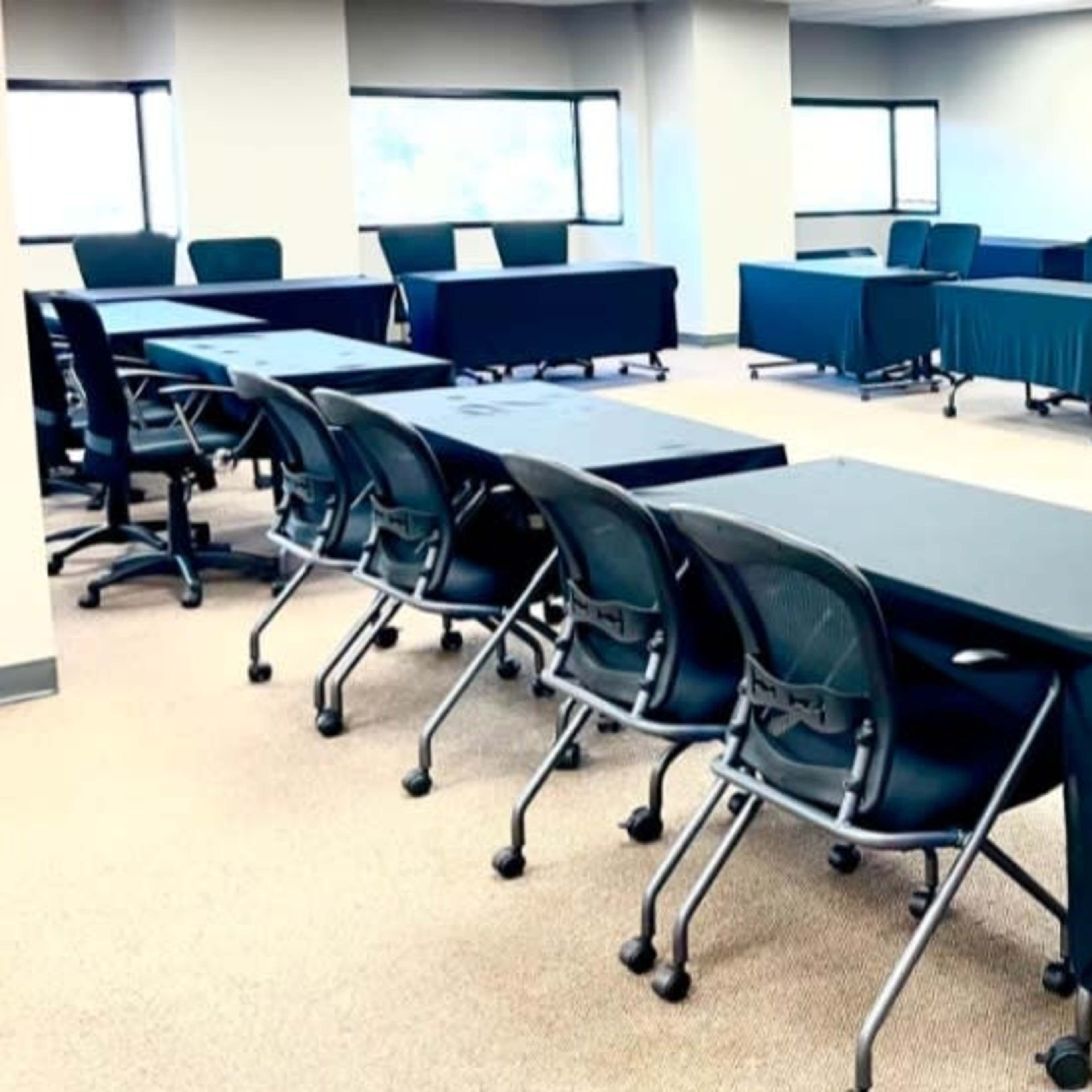 A spacious meeting room with multiple tables covered in black cloth and chairs arranged around them.
