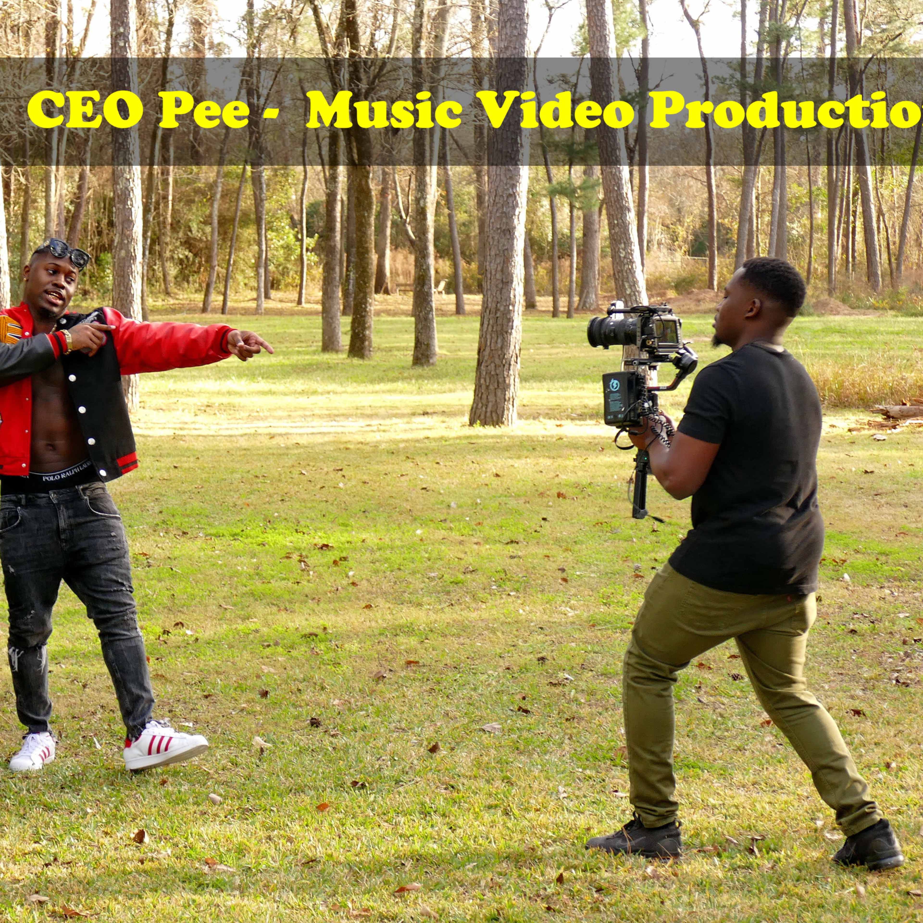 A man gestures while standing beside a tractor in a wooded area, as a woman sits on the tractor and another man films the scene with a camera.