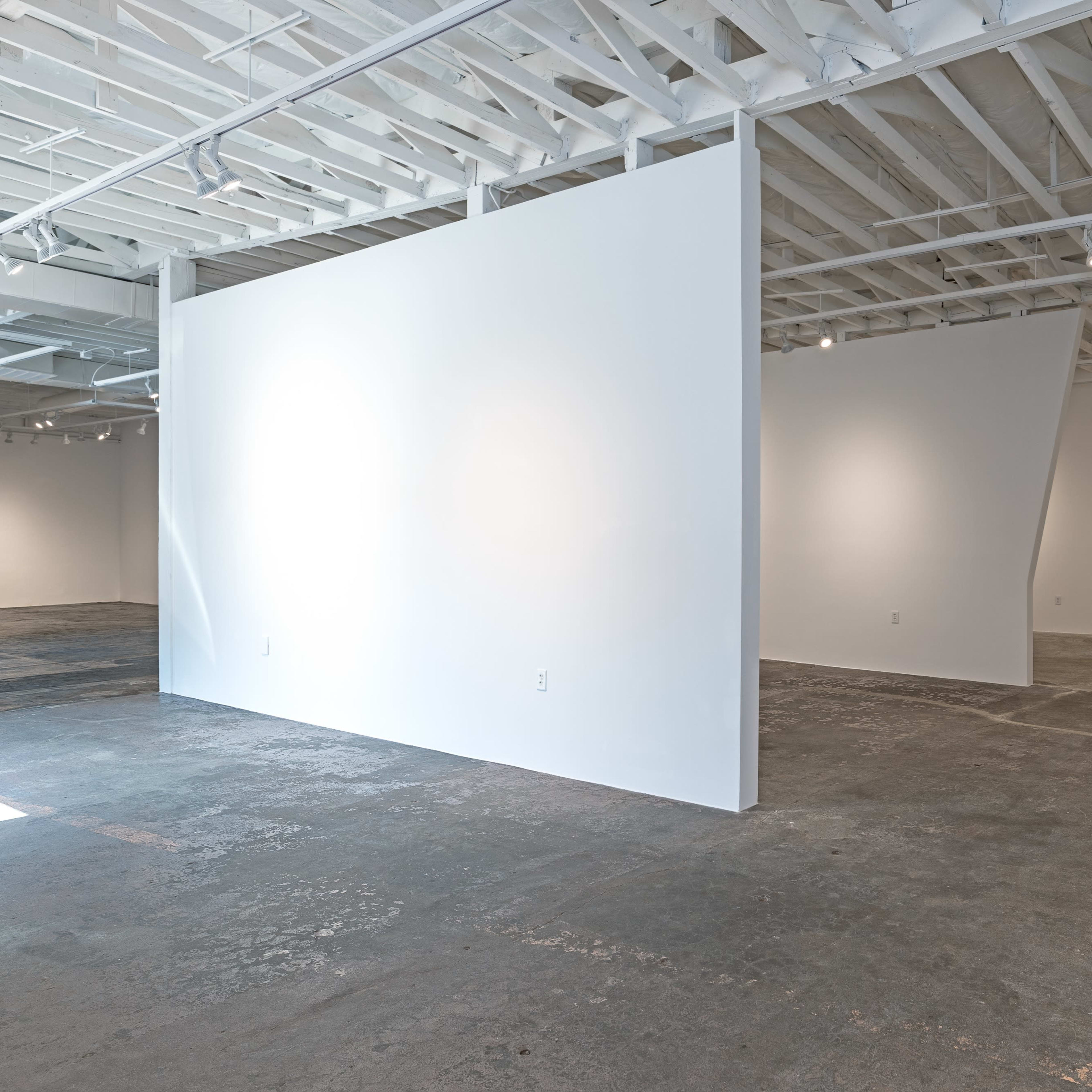 A minimalist art gallery features white walls and a concrete floor, with varying angles and lighting throughout the space.