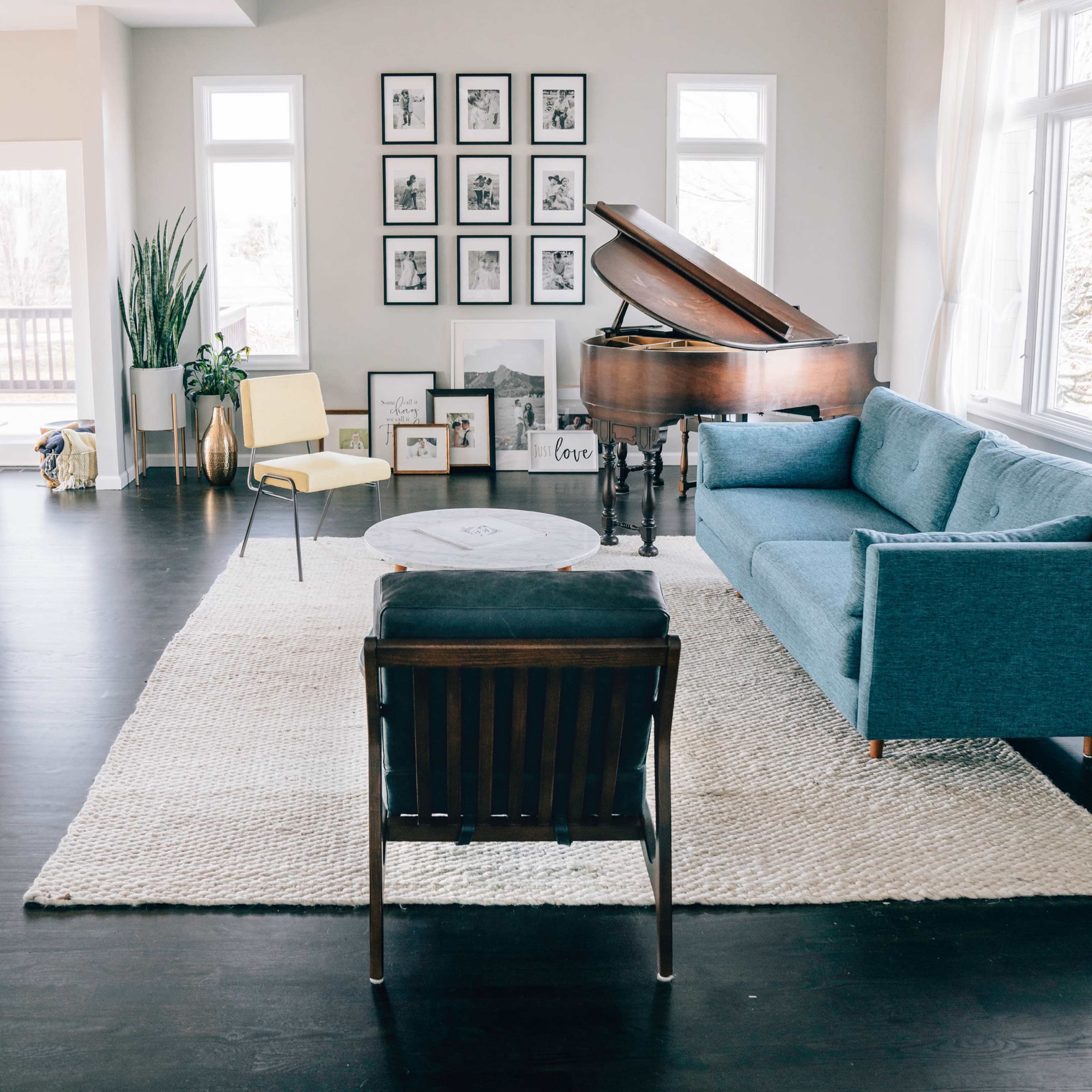 A spacious living room features a grand piano, a blue sofa, a coffee table, and a wall adorned with framed photos.
