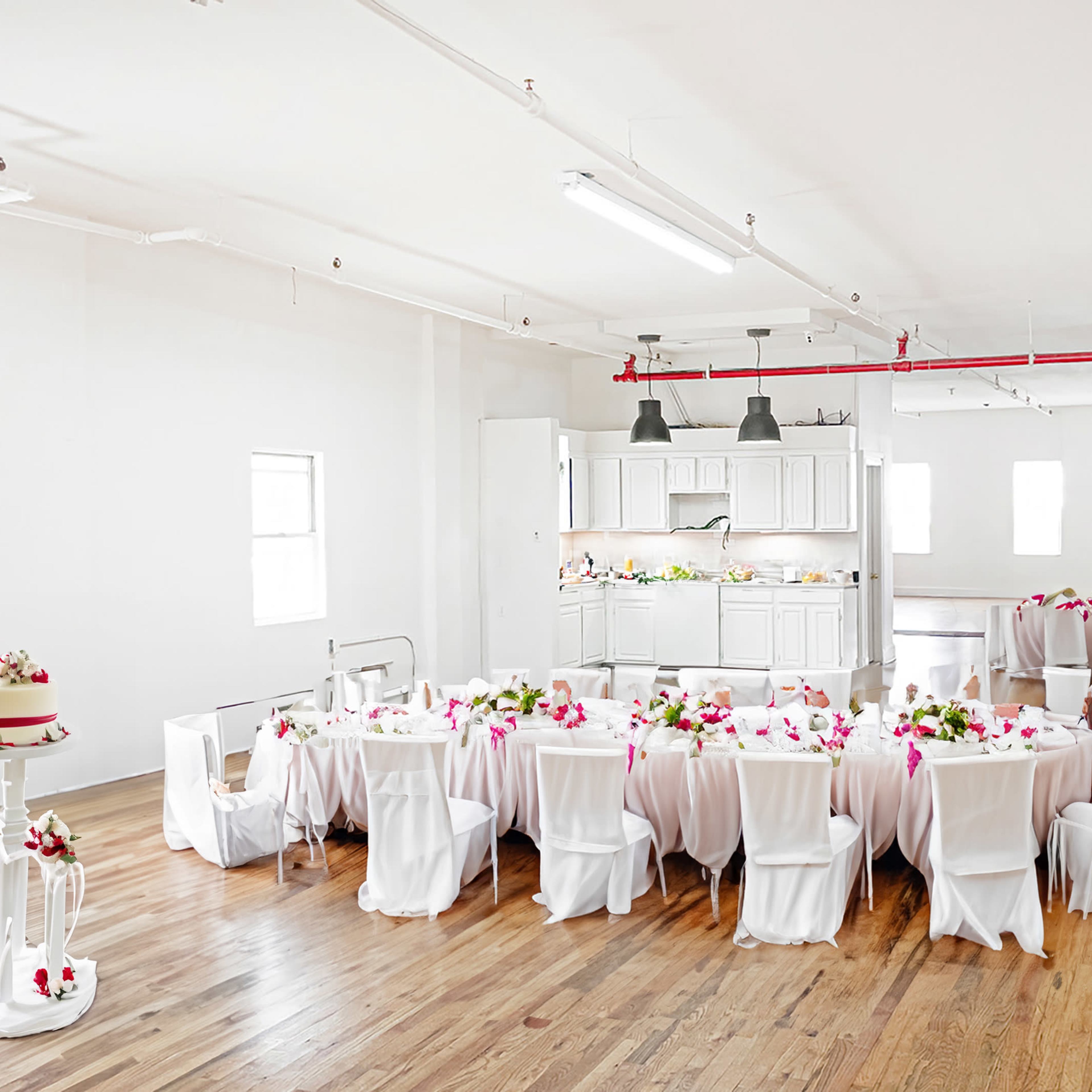 A large, elegantly set table with white tablecloths and floral centerpieces occupies a bright, open space with wooden floors and white walls.