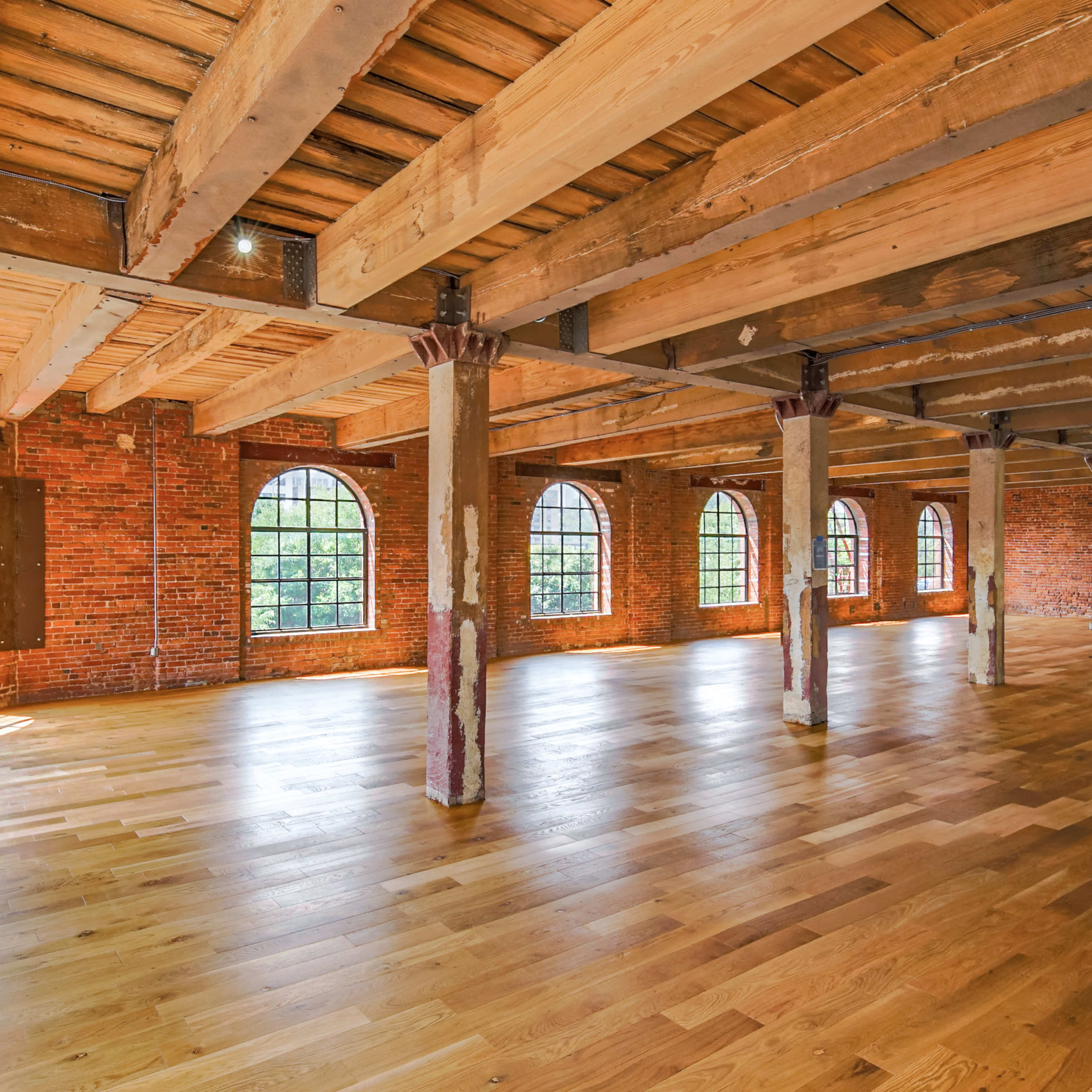 A spacious interior of a building with exposed brick walls, large windows, and wooden flooring.
