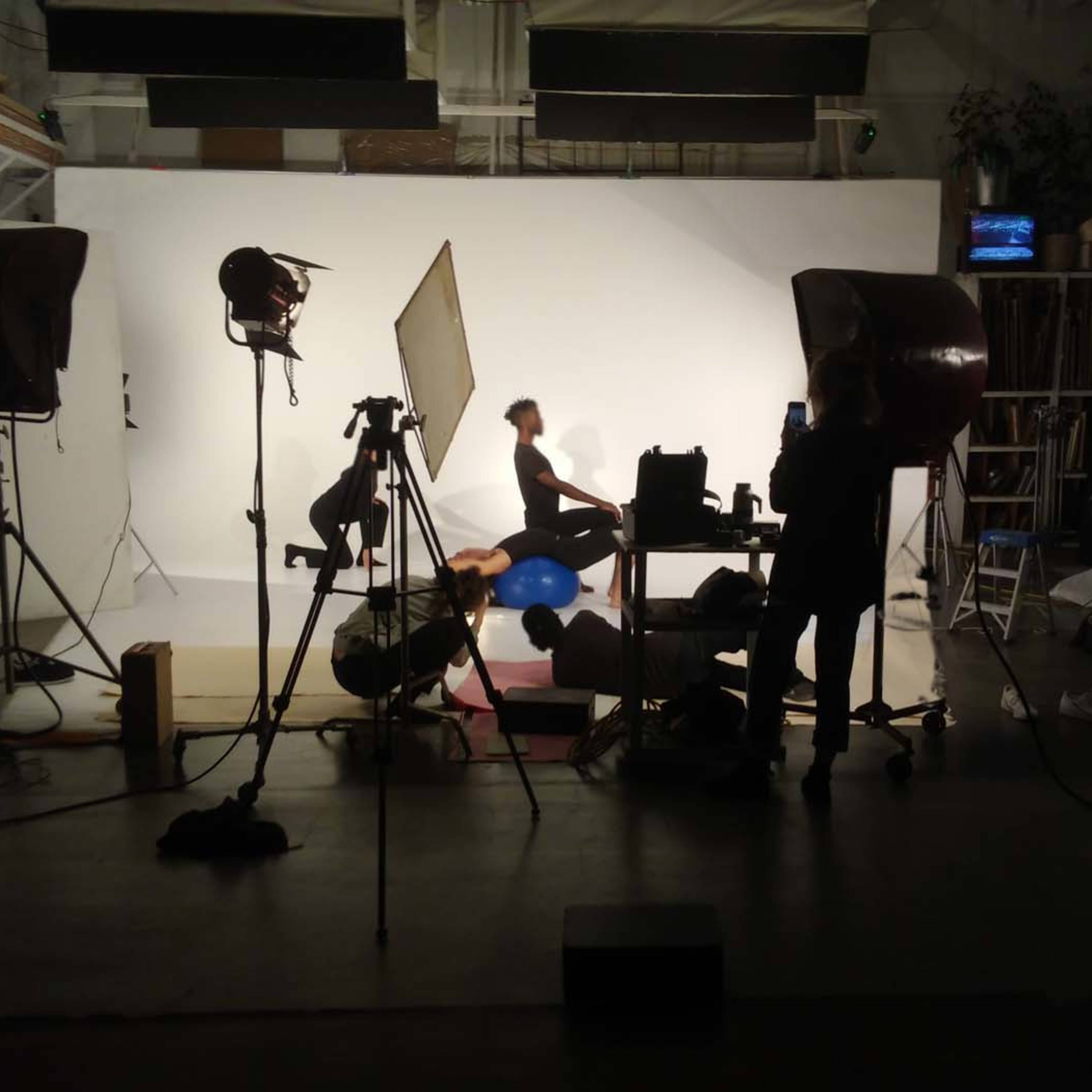 A photography studio setup with multiple lights, a backdrop, props, and individuals posing and adjusting props on set.