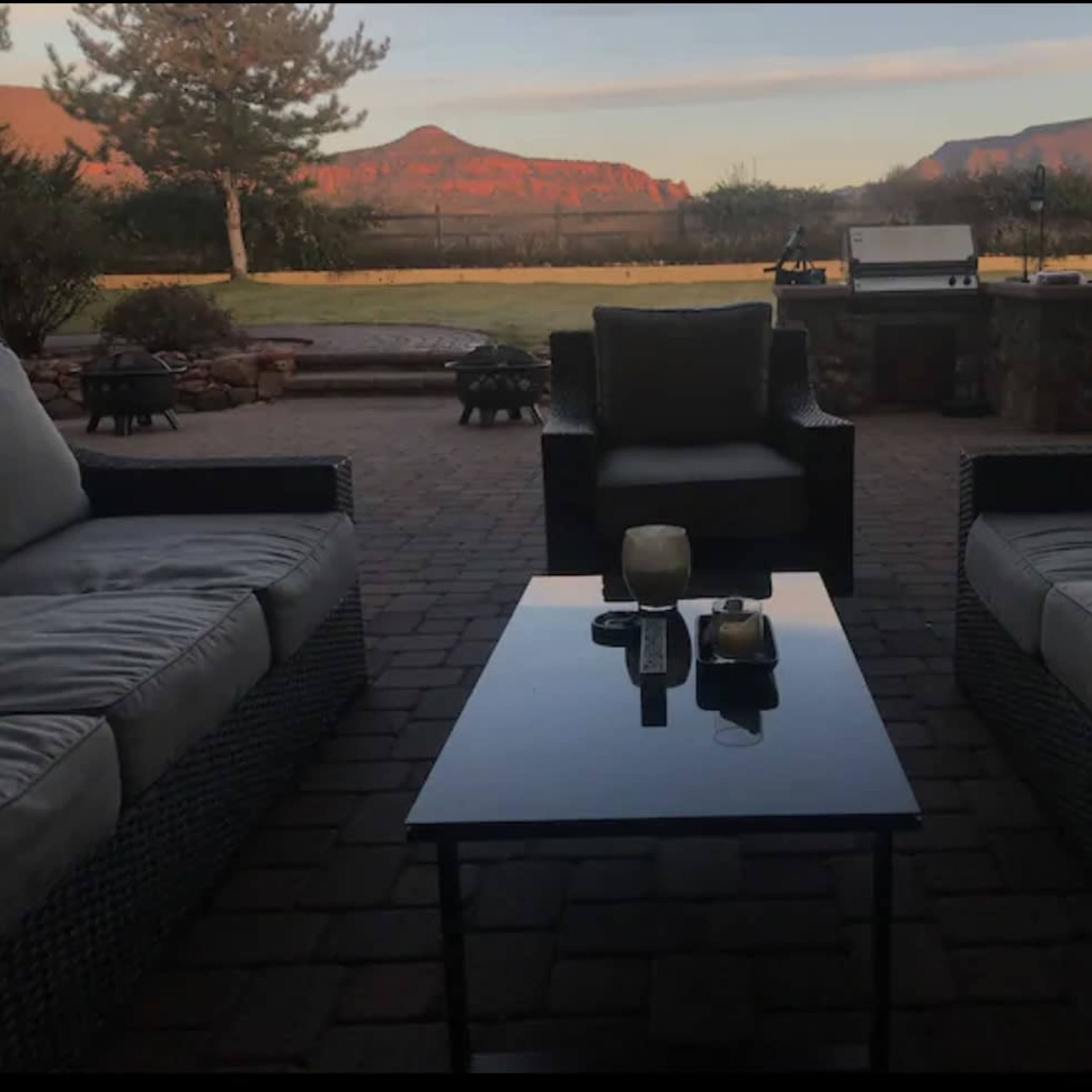 A patio area features two couches and a glass coffee table, with red rock formations in the background under a clear sky.