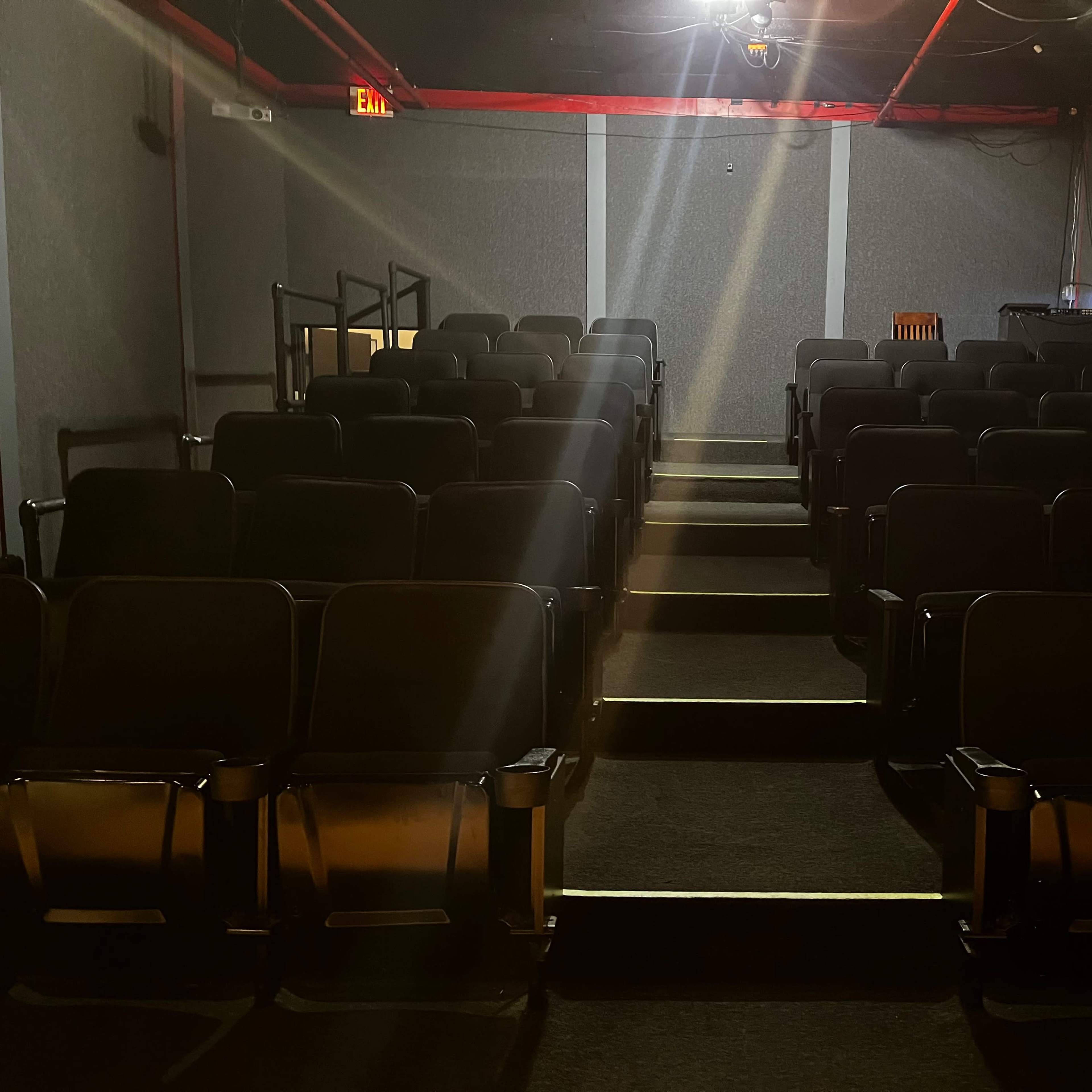 An empty movie theater with rows of black seats and dim lighting.