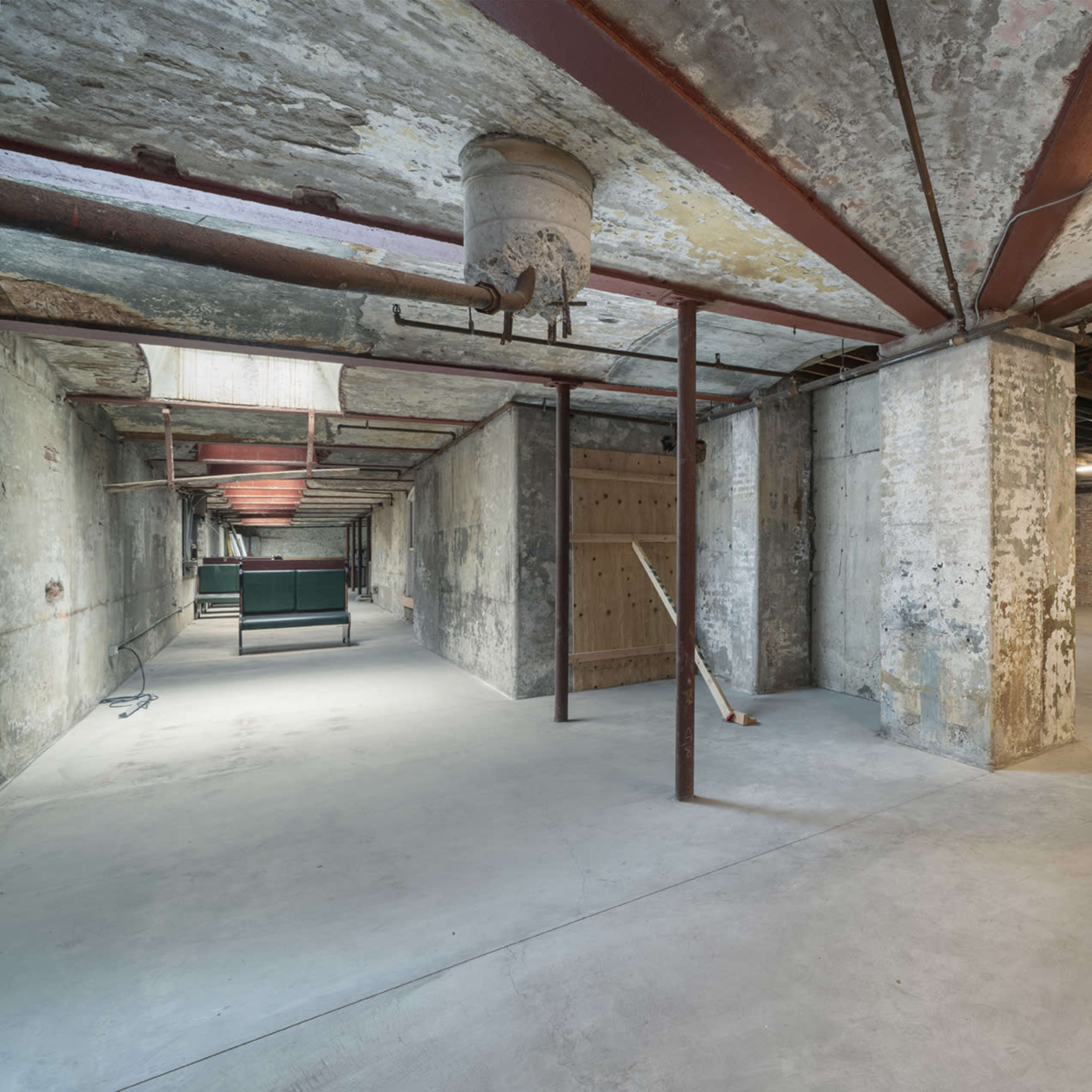 A large, empty basement space with exposed concrete walls, metal pillars, and a few overhead lights illuminating the area.