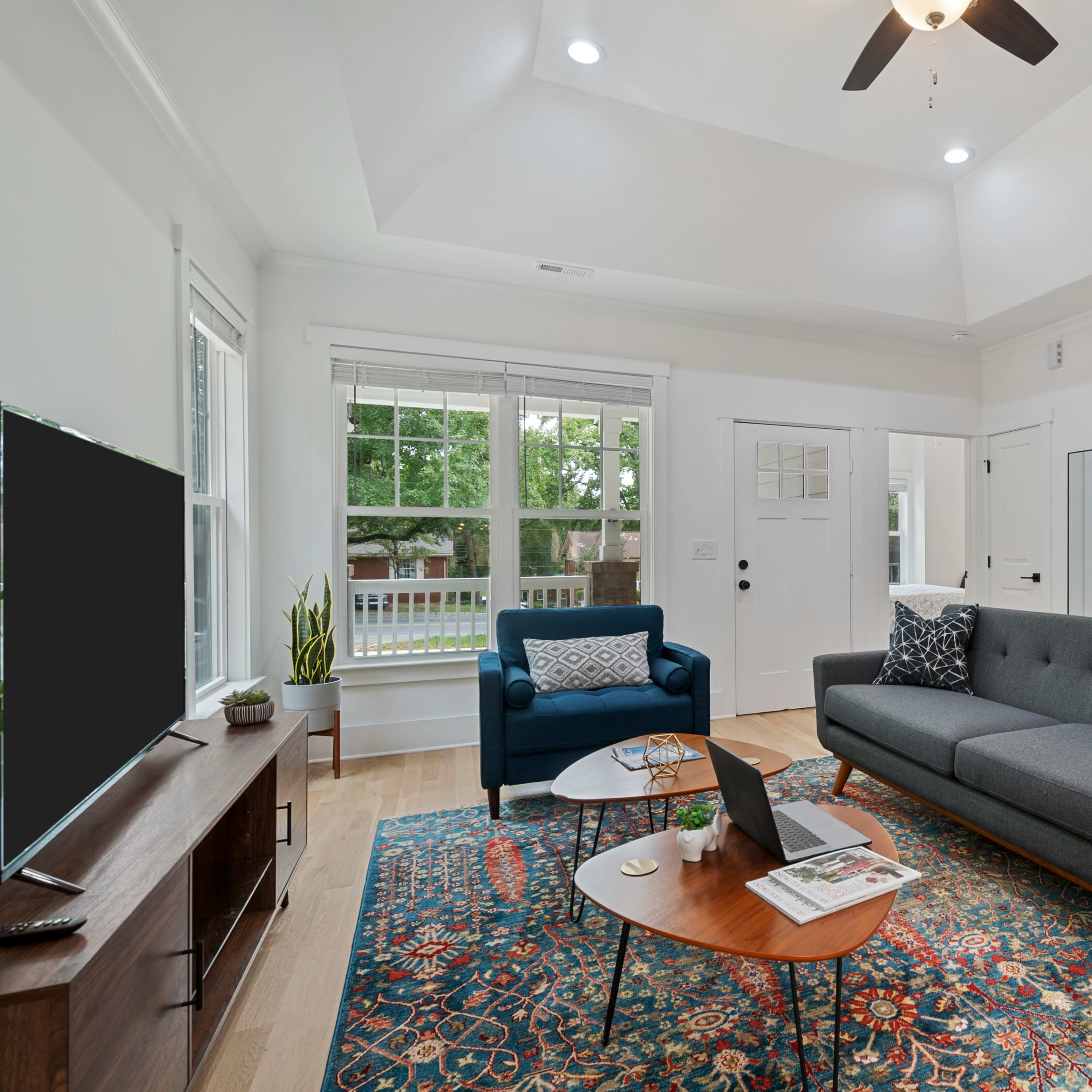 A modern living room featuring a gray sectional sofa, an accent chair, a coffee table, and two artwork pieces on the walls, illuminated by natural light from the windows.