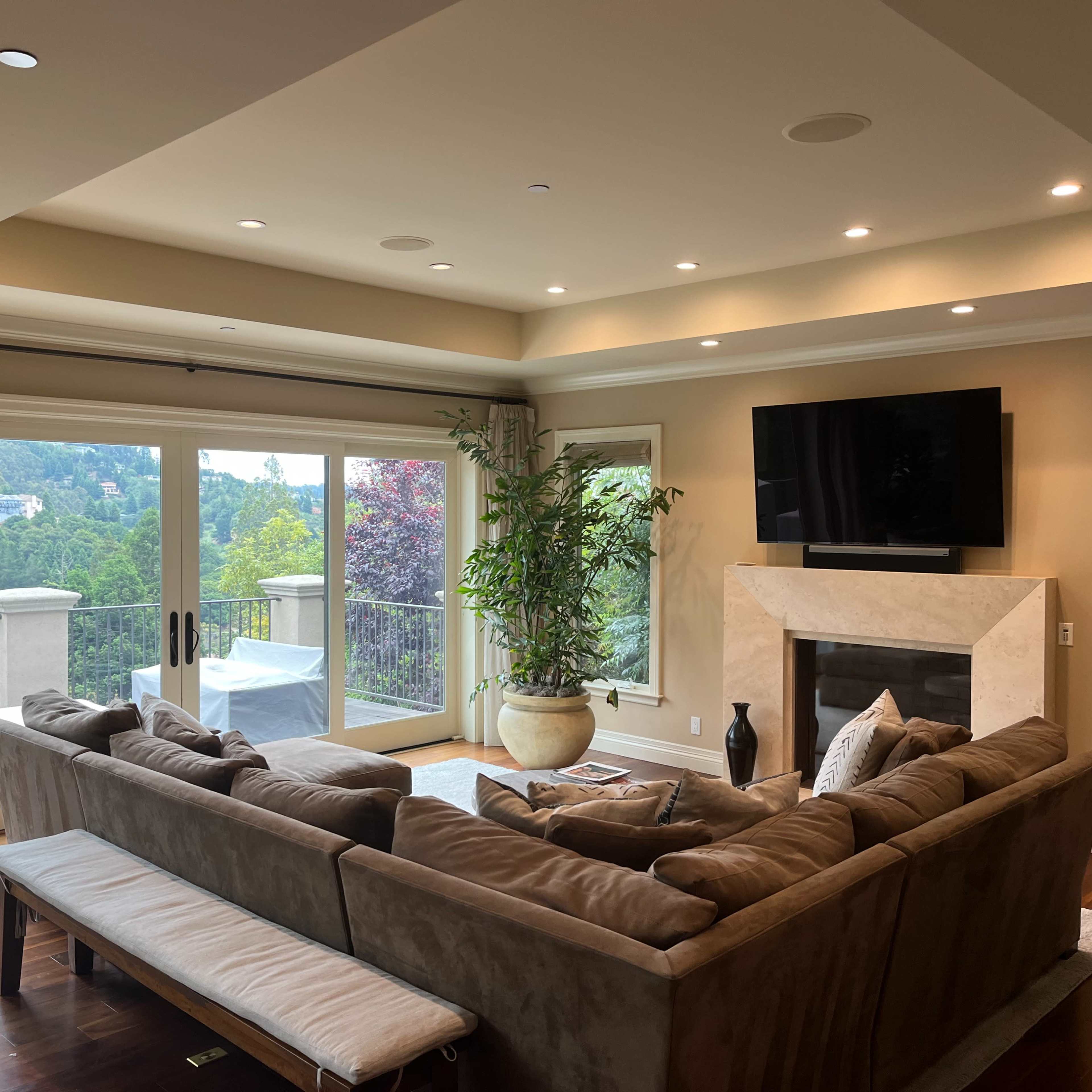 A spacious living room with a large sectional sofa, a TV mounted on the wall, and sliding glass doors leading to a balcony with a scenic view.