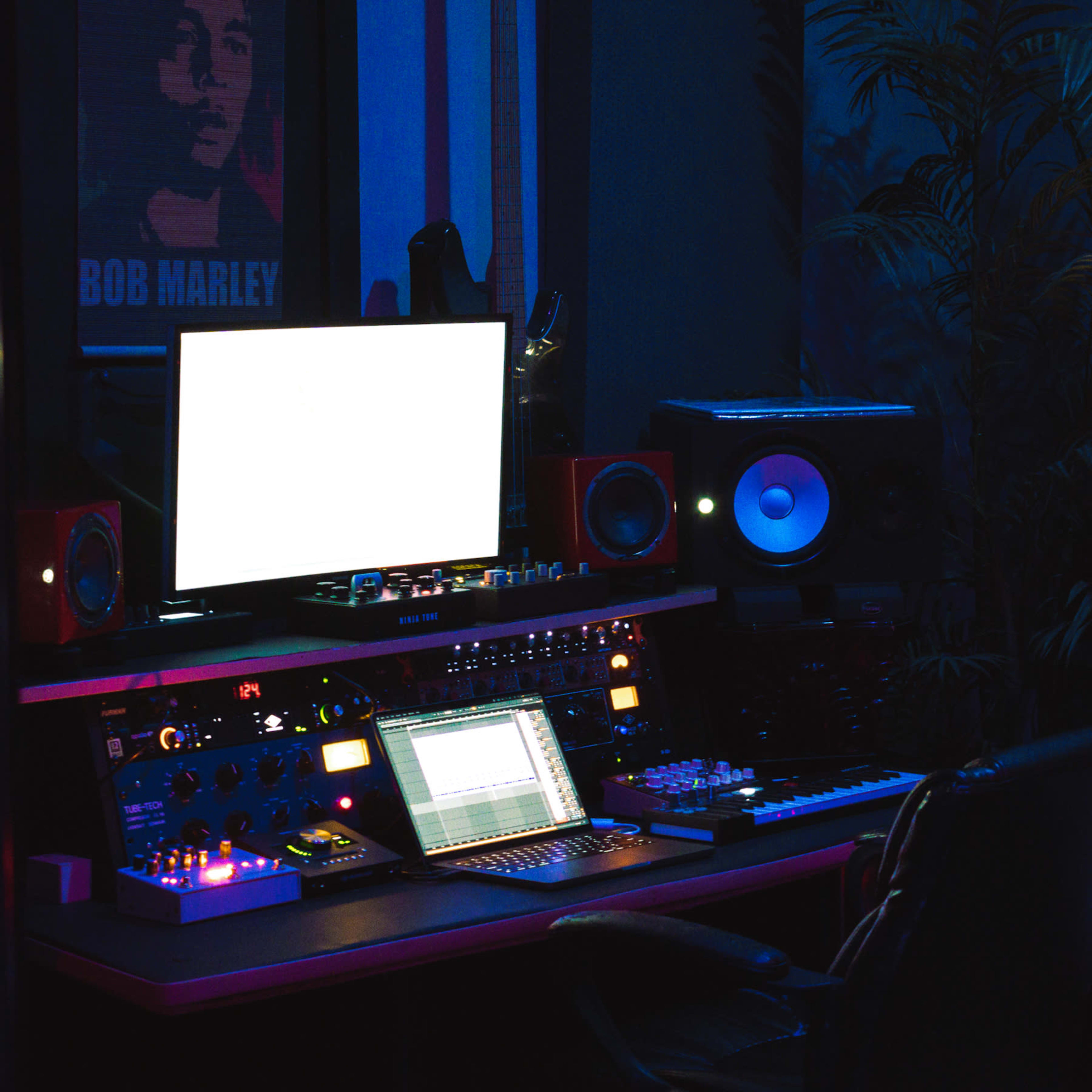 A dimly lit music studio features a mixing console, computer, and various musical equipment, with a poster of Bob Marley on the wall.