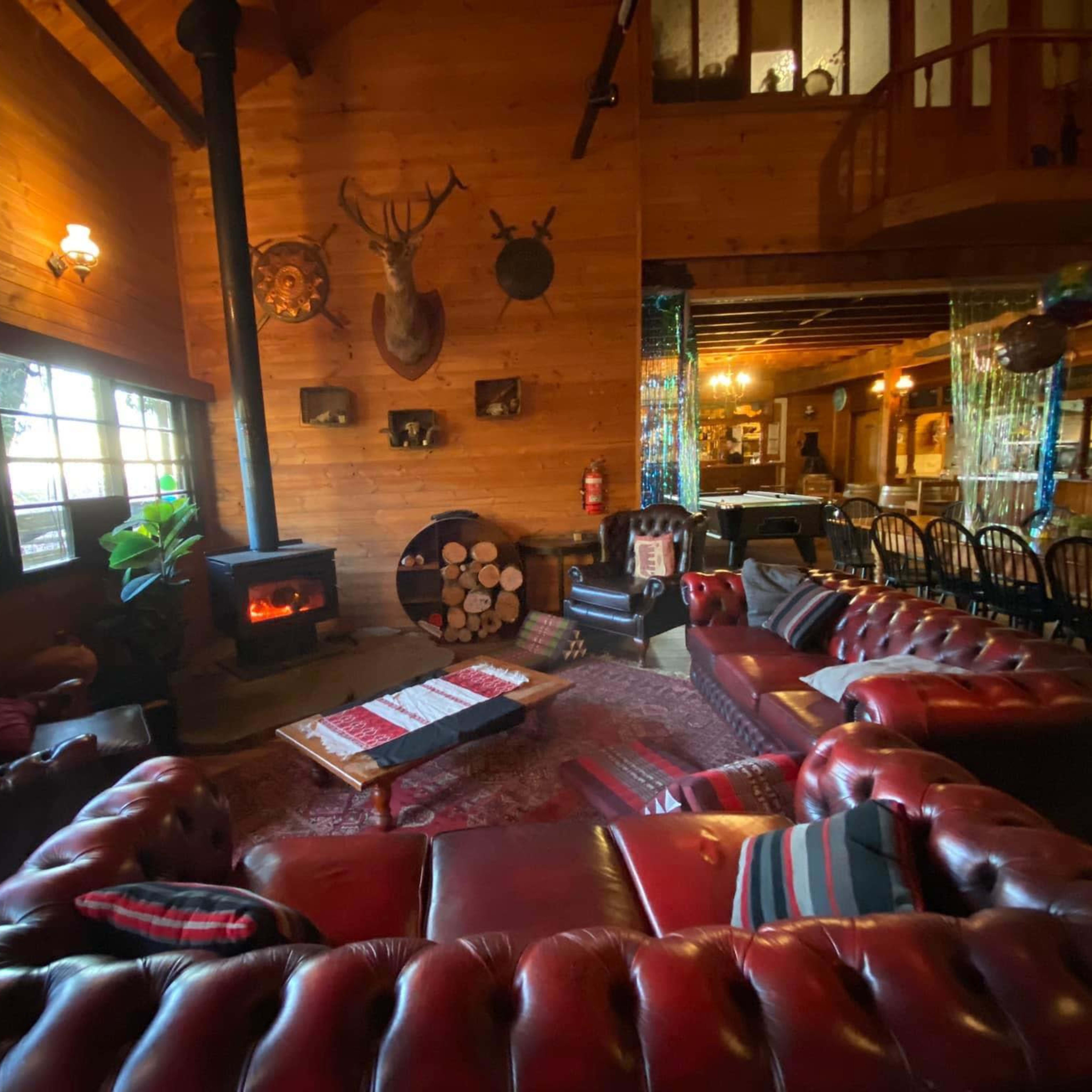 A cozy wooden lounge with leather sofas arranged around a coffee table, a stove, and various decorative elements on the walls.
