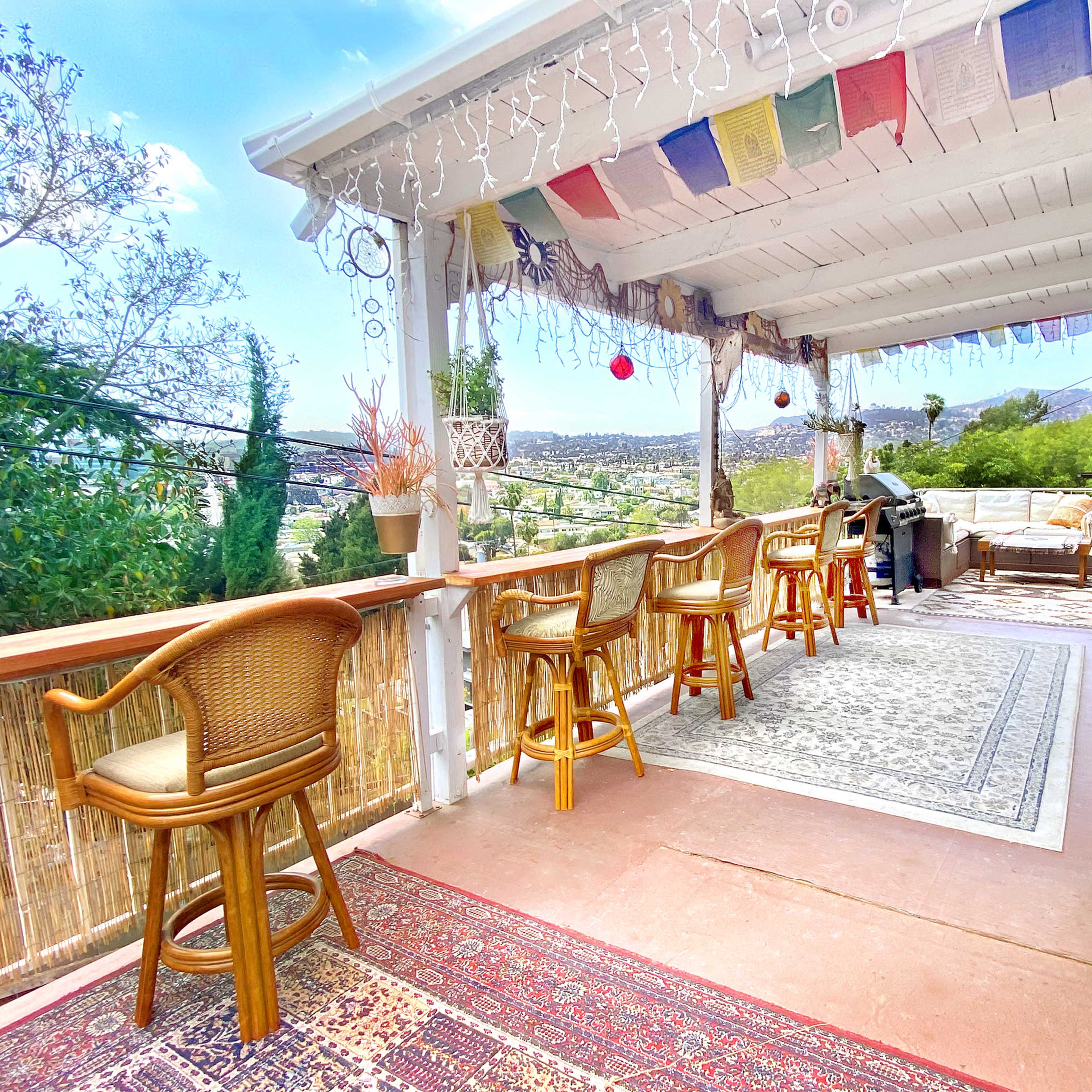 A spacious outdoor porch decorated with hanging lights, colorful banners, and seating areas overlooking a scenic landscape.