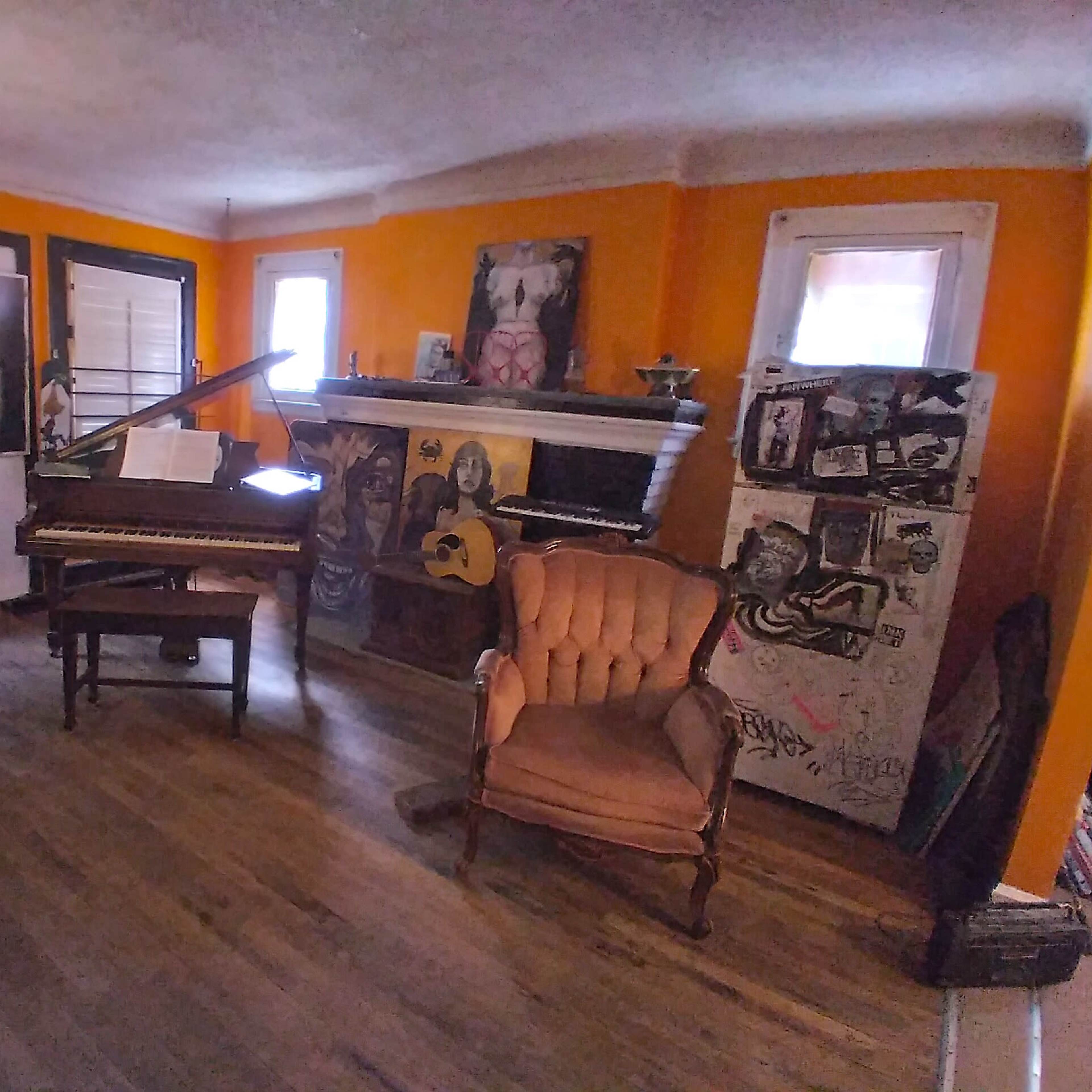 A colorful room with a piano, a vintage armchair, a dining table with chairs, and eclectic artwork on the walls.