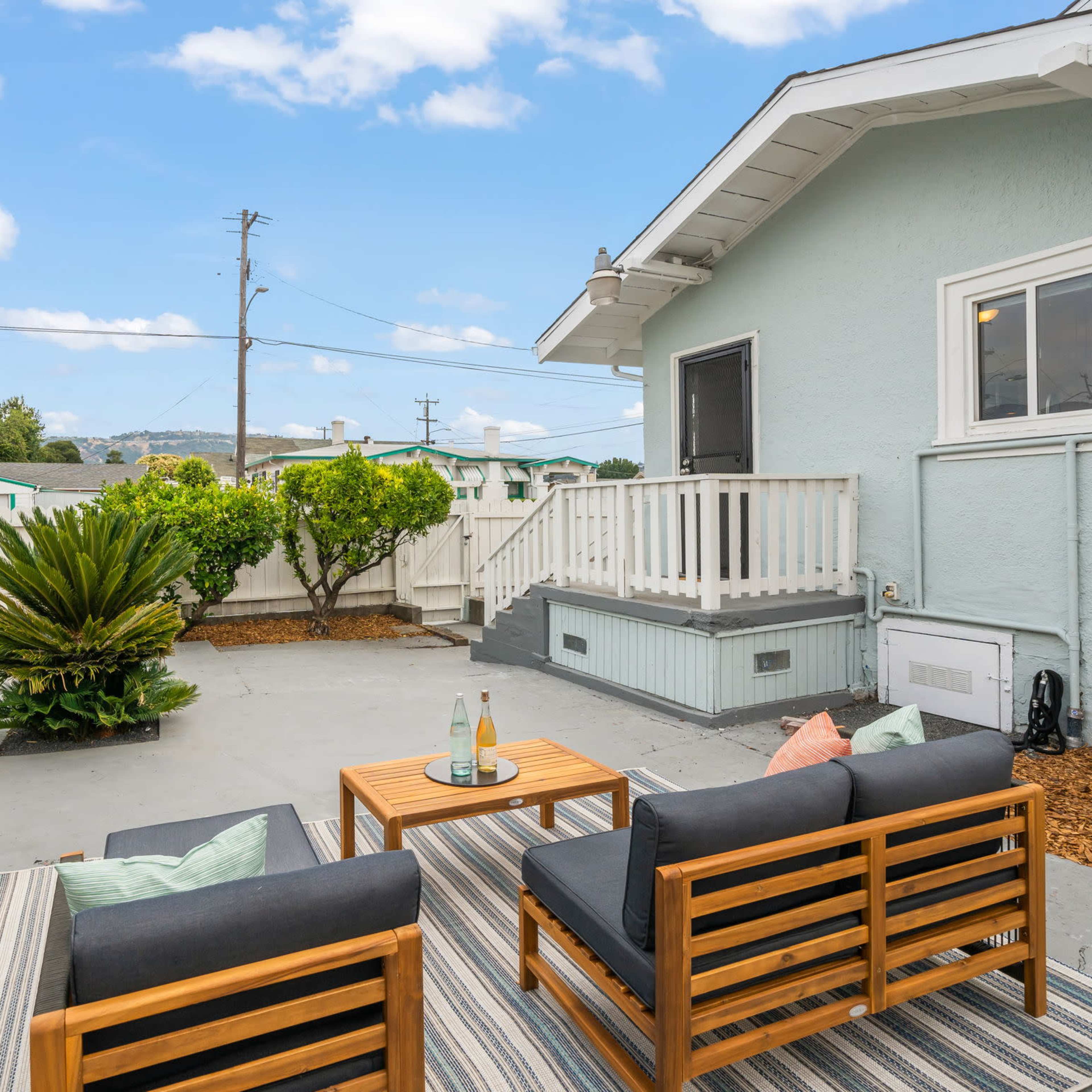 An outdoor seating area with two wooden chairs and a coffee table, surrounded by a small garden and a fenced yard.