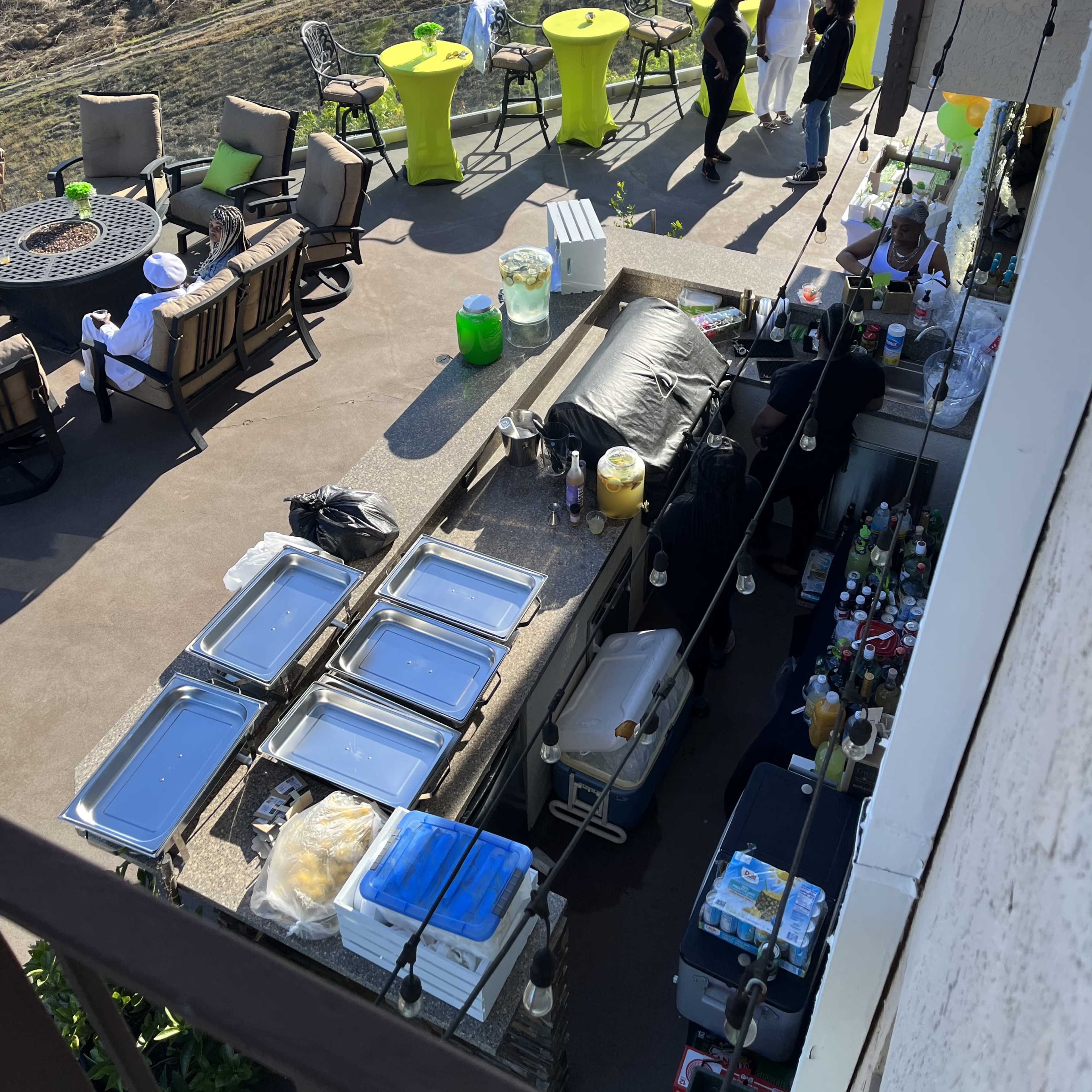 An outdoor event setup with tables and chairs, featuring a bar area stocked with various drinks and food containers.