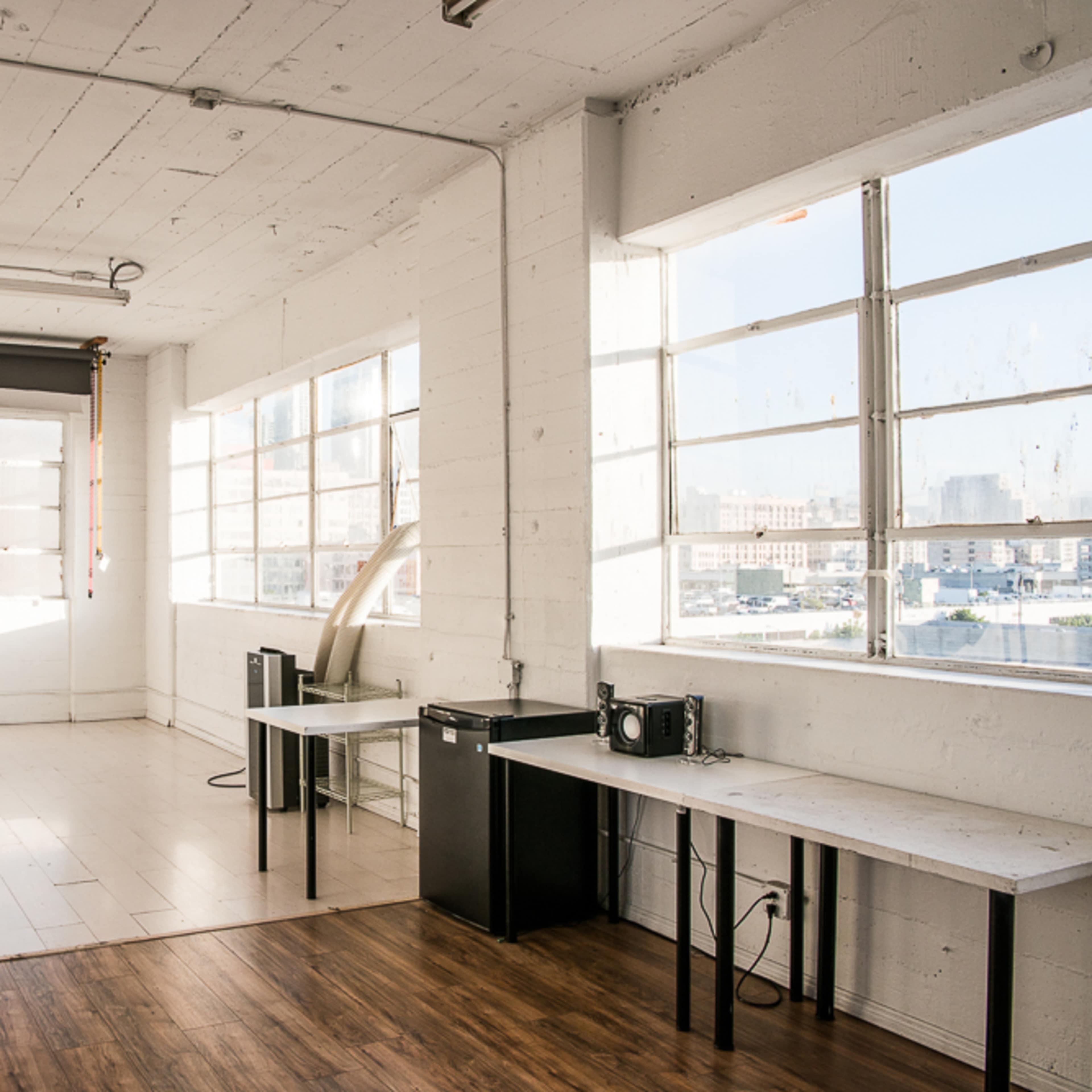 A spacious studio room with large windows, light wooden floors, and photography equipment in one corner.