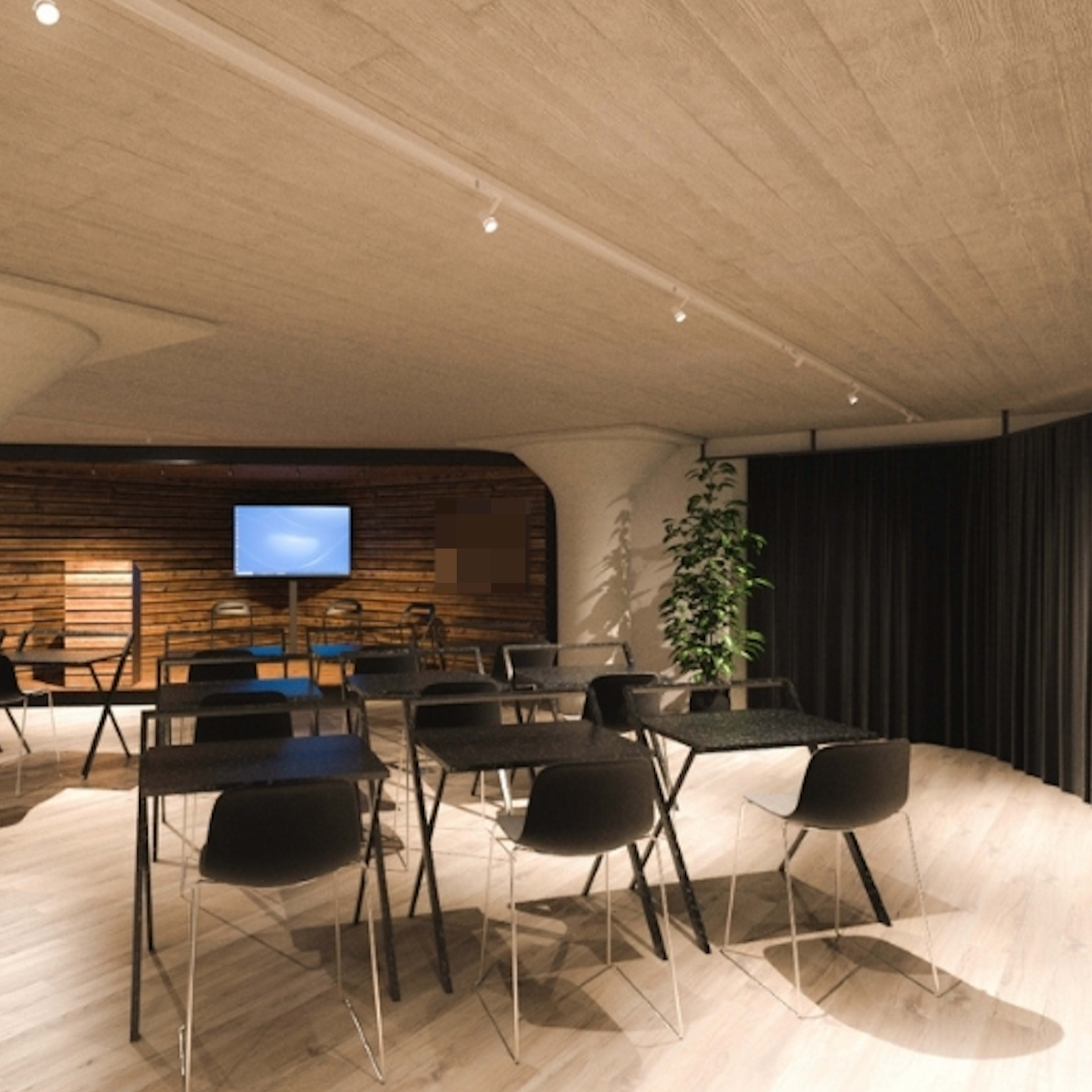 A modern classroom or event space with black folding tables and chairs arranged in a semi-circle, featuring a television screen and wooden paneling in the background.