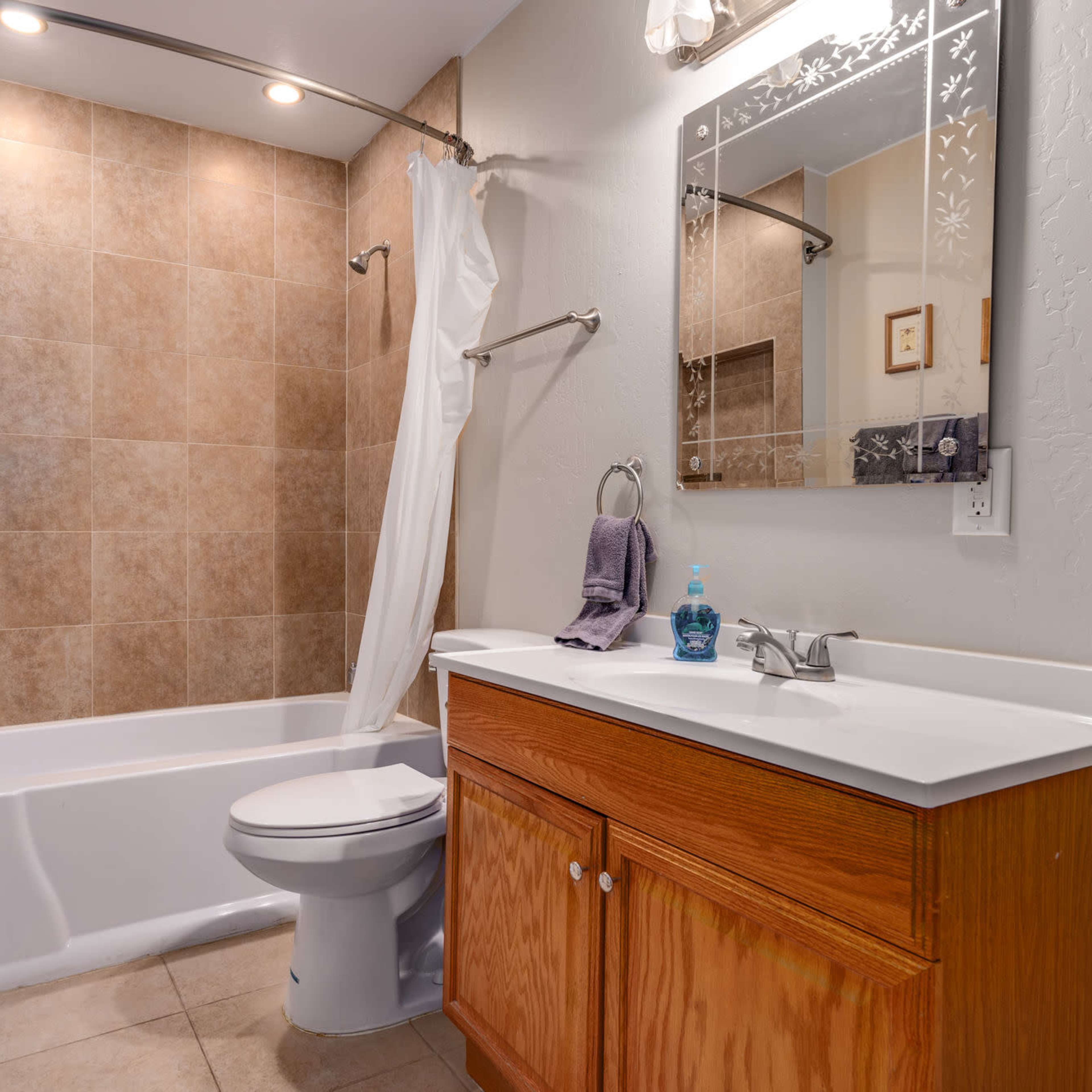 A small bathroom featuring a bathtub with a shower curtain, a toilet, a wooden vanity with a sink, and tiled walls.