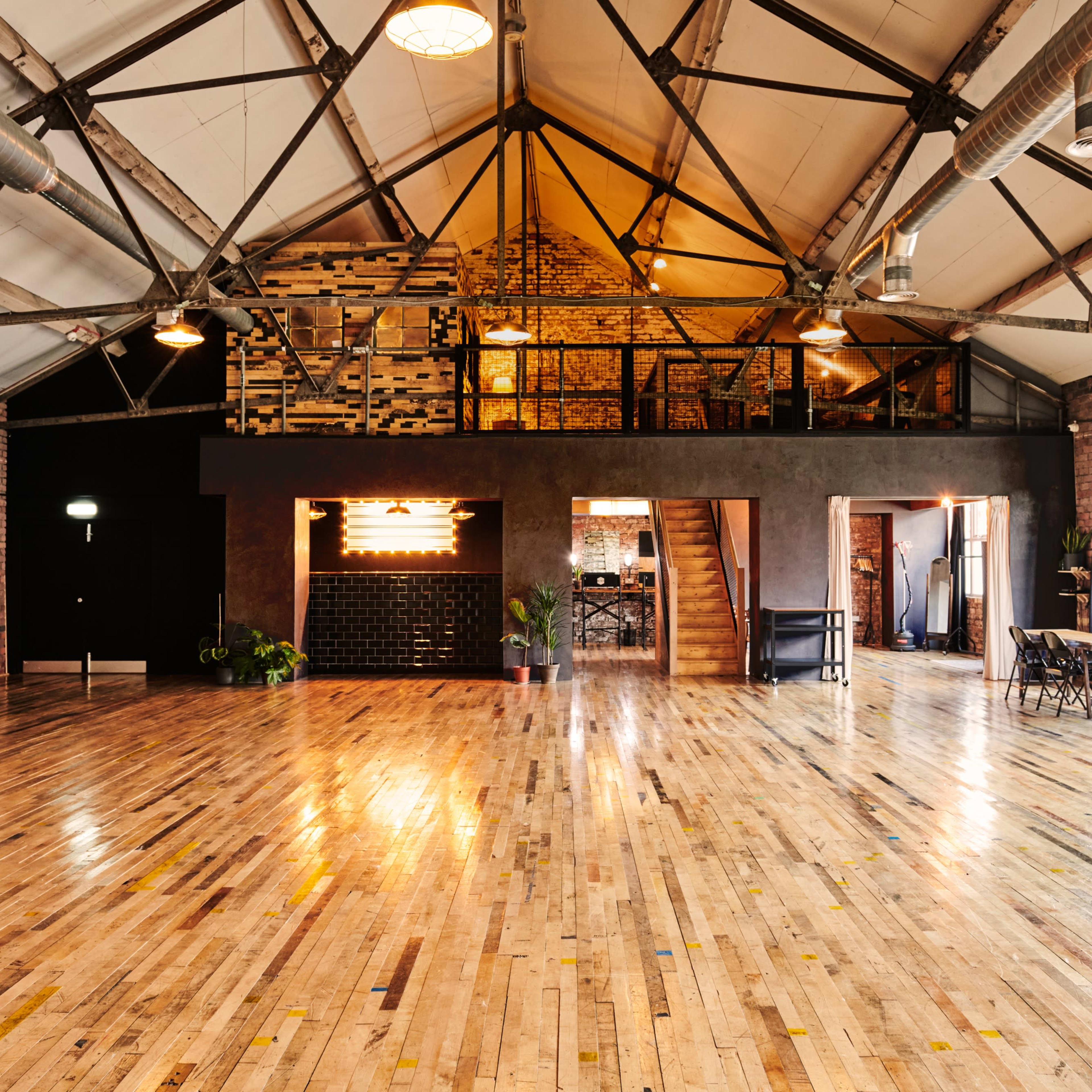 An industrial-style event space with high ceilings, exposed brick walls, and polished wooden floors.
