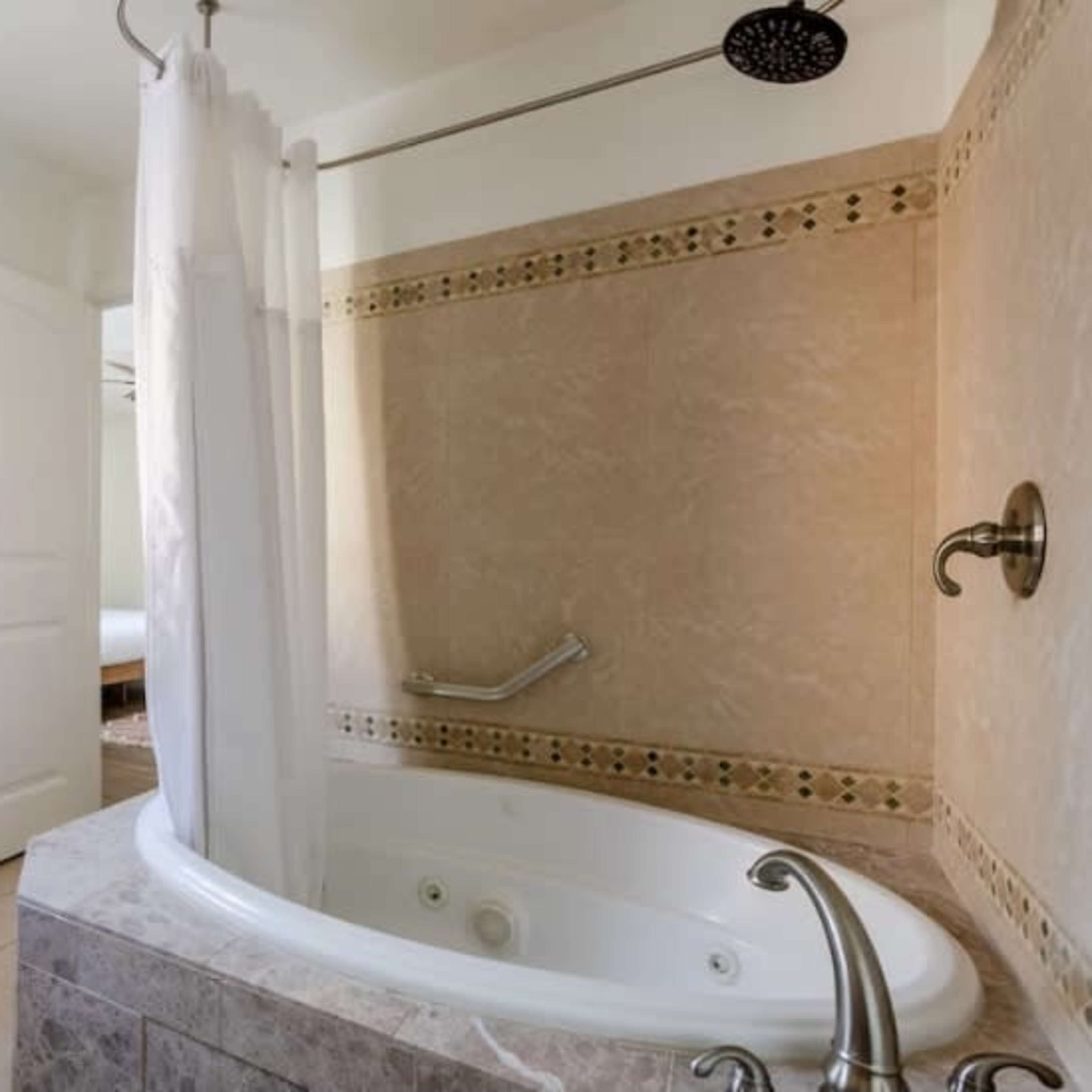 A bathroom with a corner tub, a shower curtain, and a window with sheer curtains.
