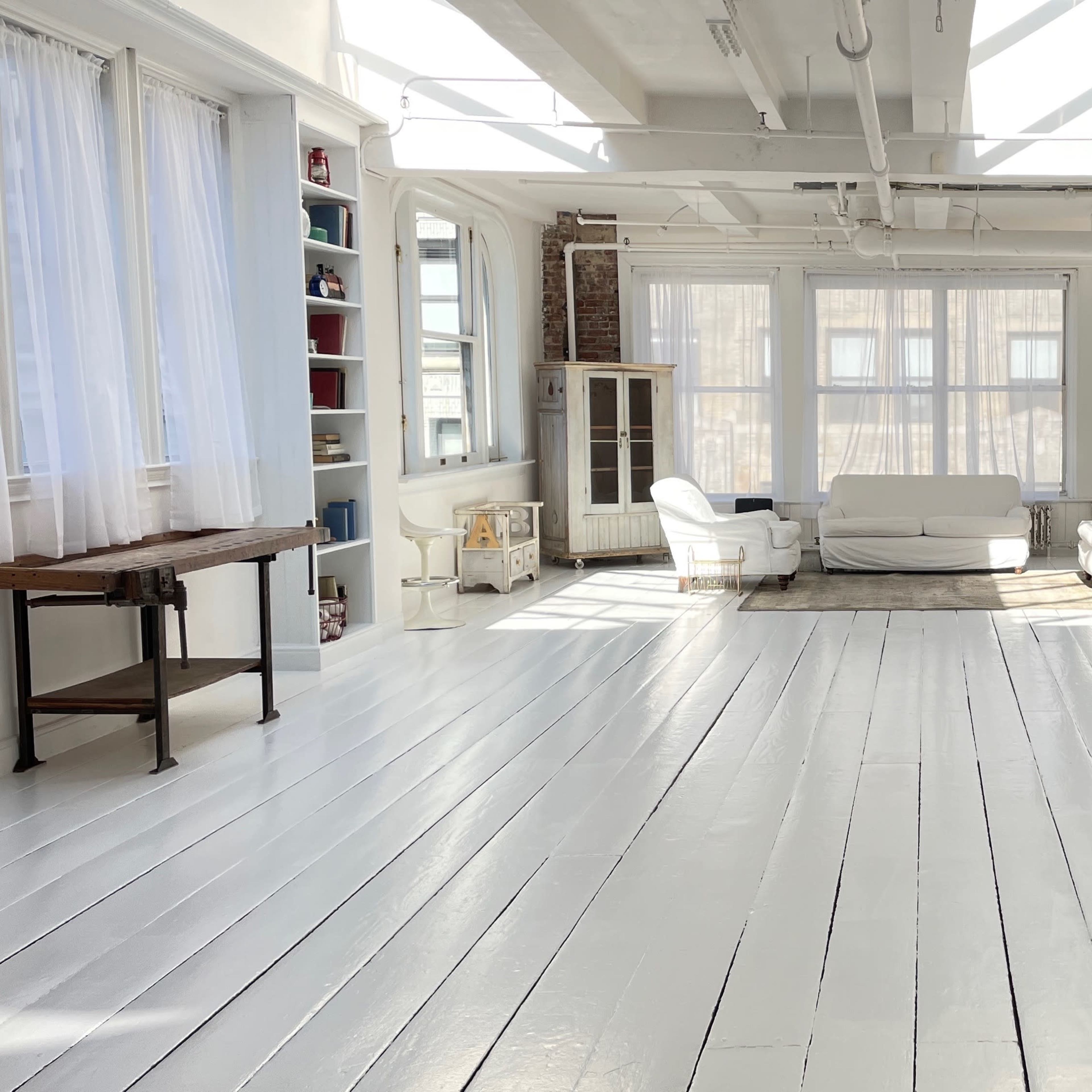 A bright, open space with white wooden floors, large windows, and minimalist furniture including a sofa and chairs.