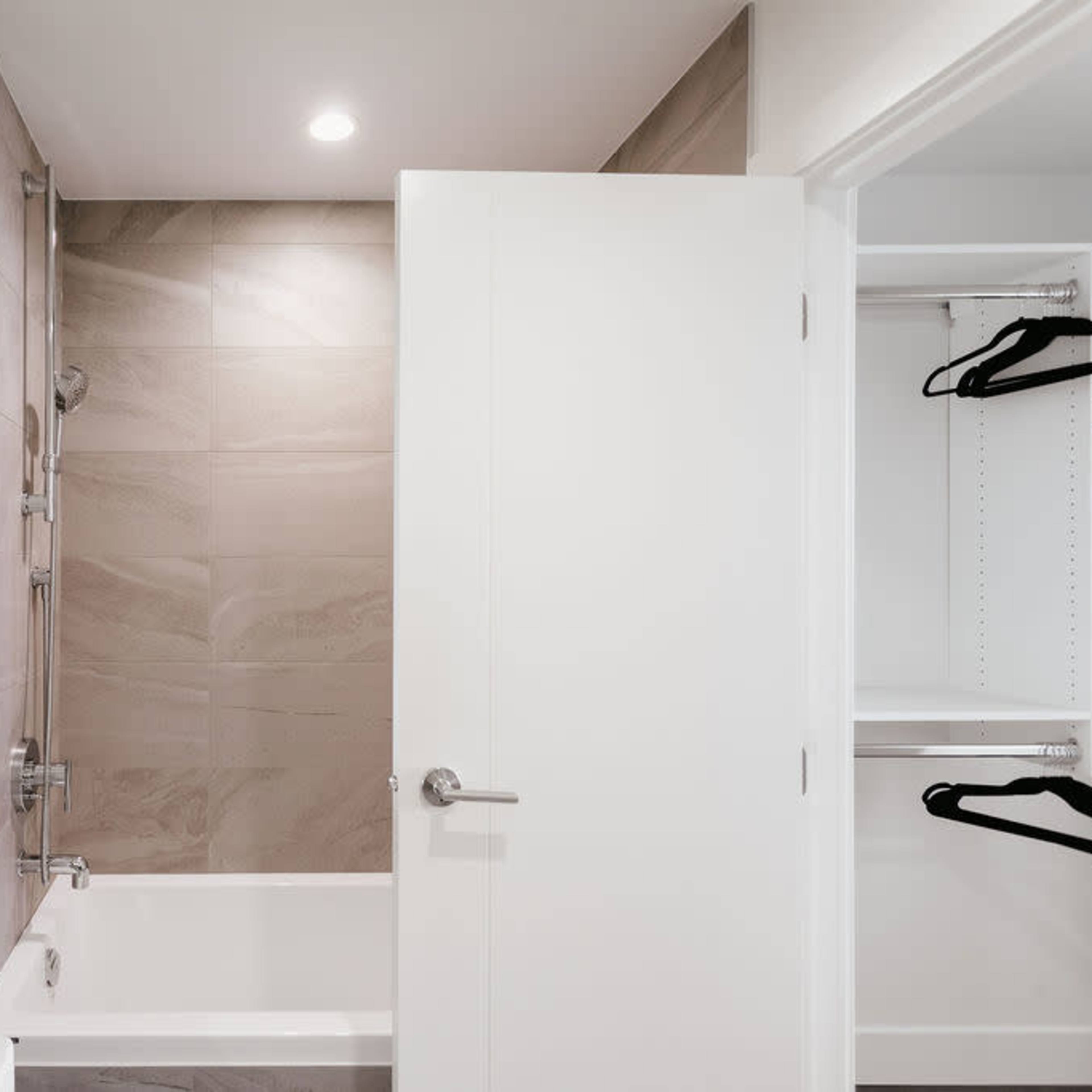 A modern bathroom featuring a bathtub, a large mirror, and a closet with hanging space.