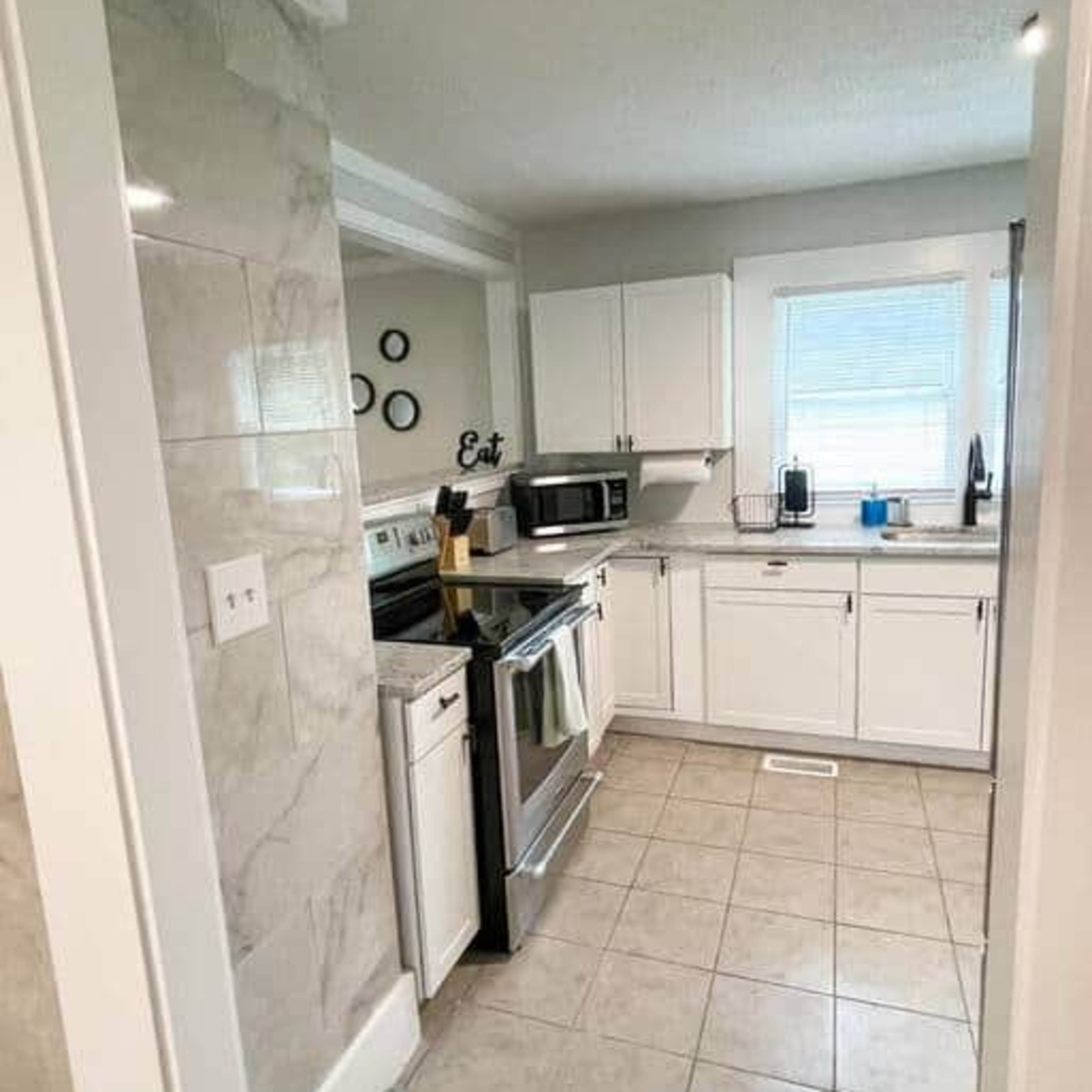 A small, bright kitchen with white cabinets, a stainless steel stove, and a window above the sink.