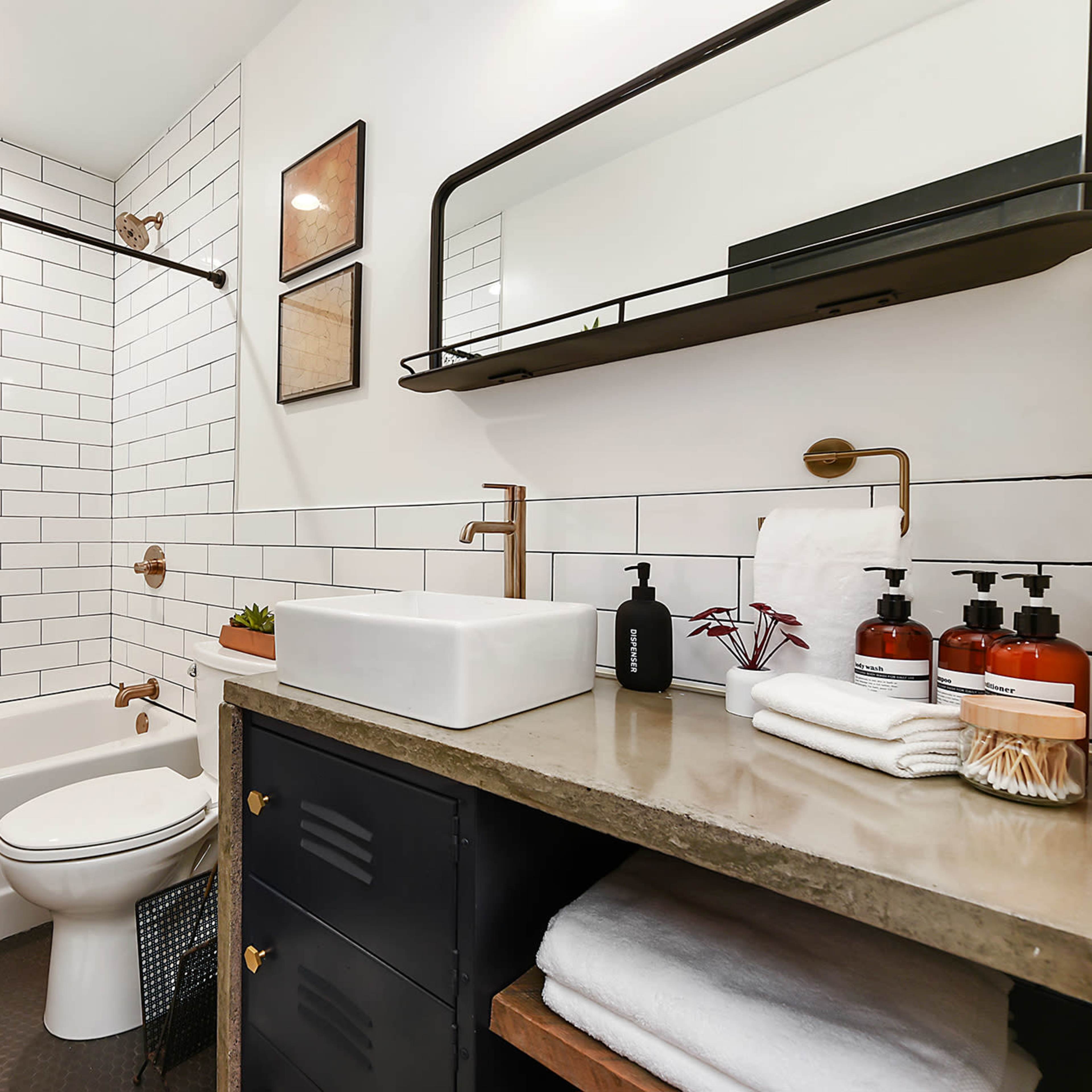 A modern bathroom featuring a white tiled shower area, a rectangular sink on a concrete countertop, and a dark cabinet with neatly arranged toiletries and towels.