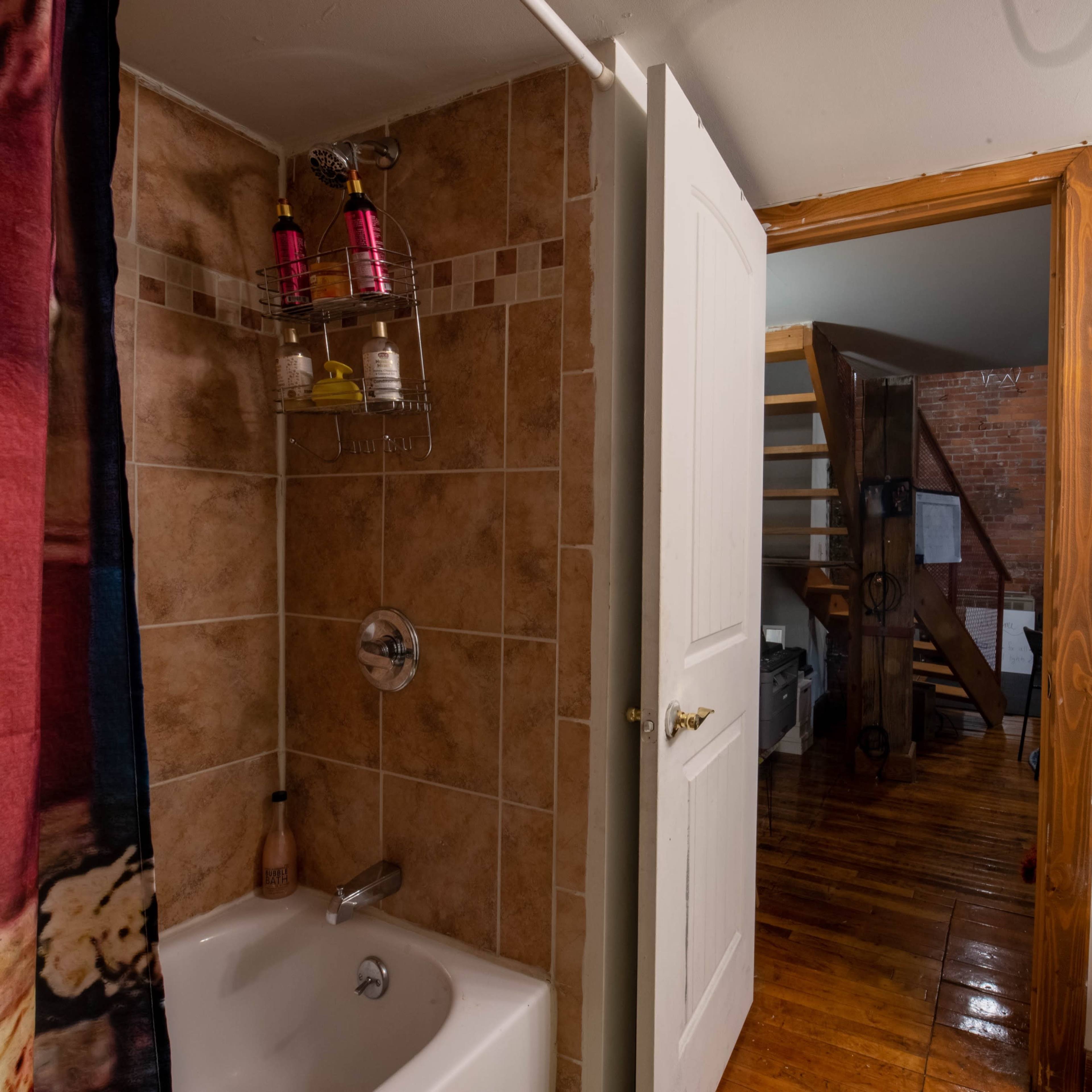 A bathroom with a shower stall, a sink area, and an open door leading to a staircase.