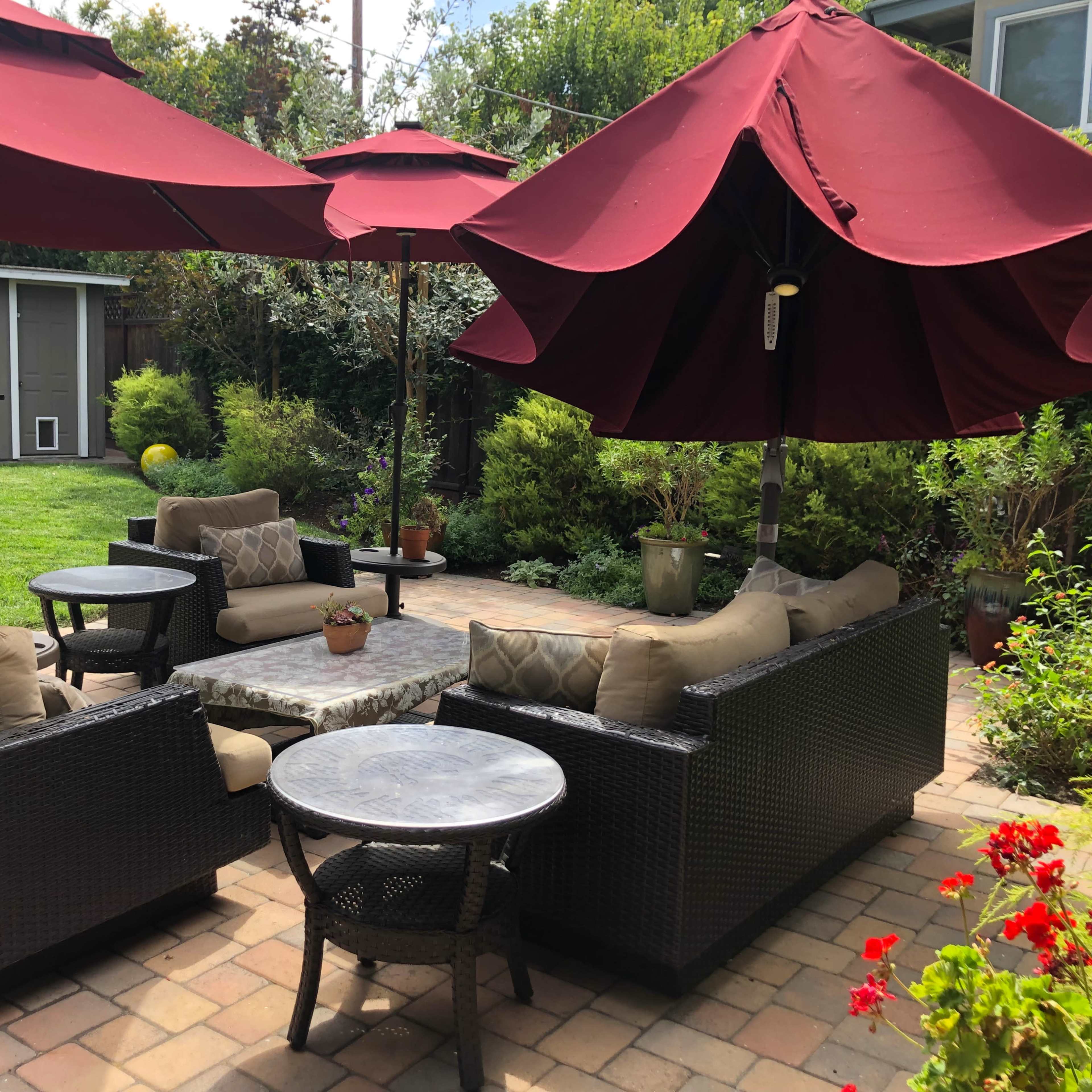 A patio seating area with two large red umbrellas, surrounded by comfortable furniture and a landscaped garden.