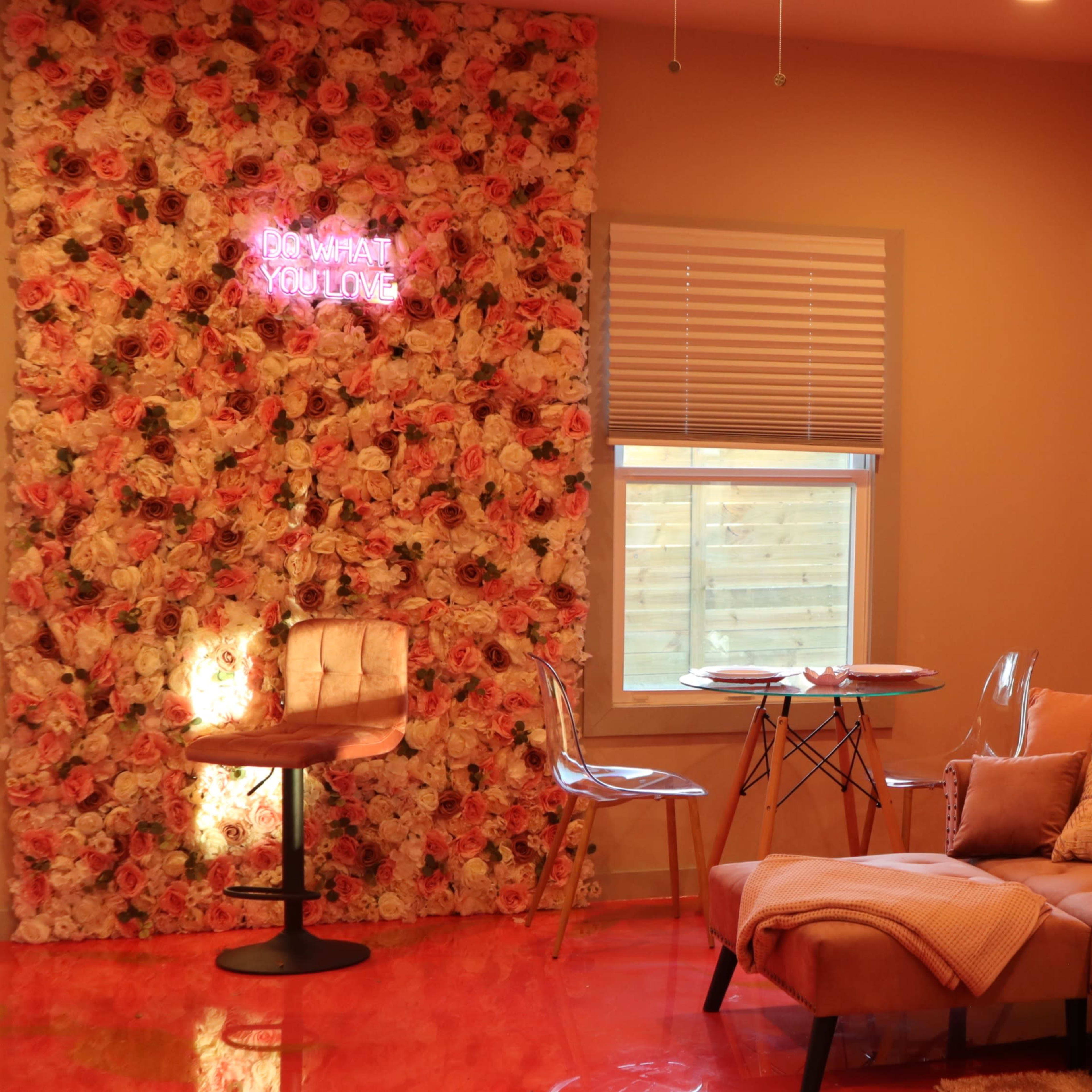 A cozy living room features a floral accent wall, a tan sectional sofa, and a small dining table with clear chairs.