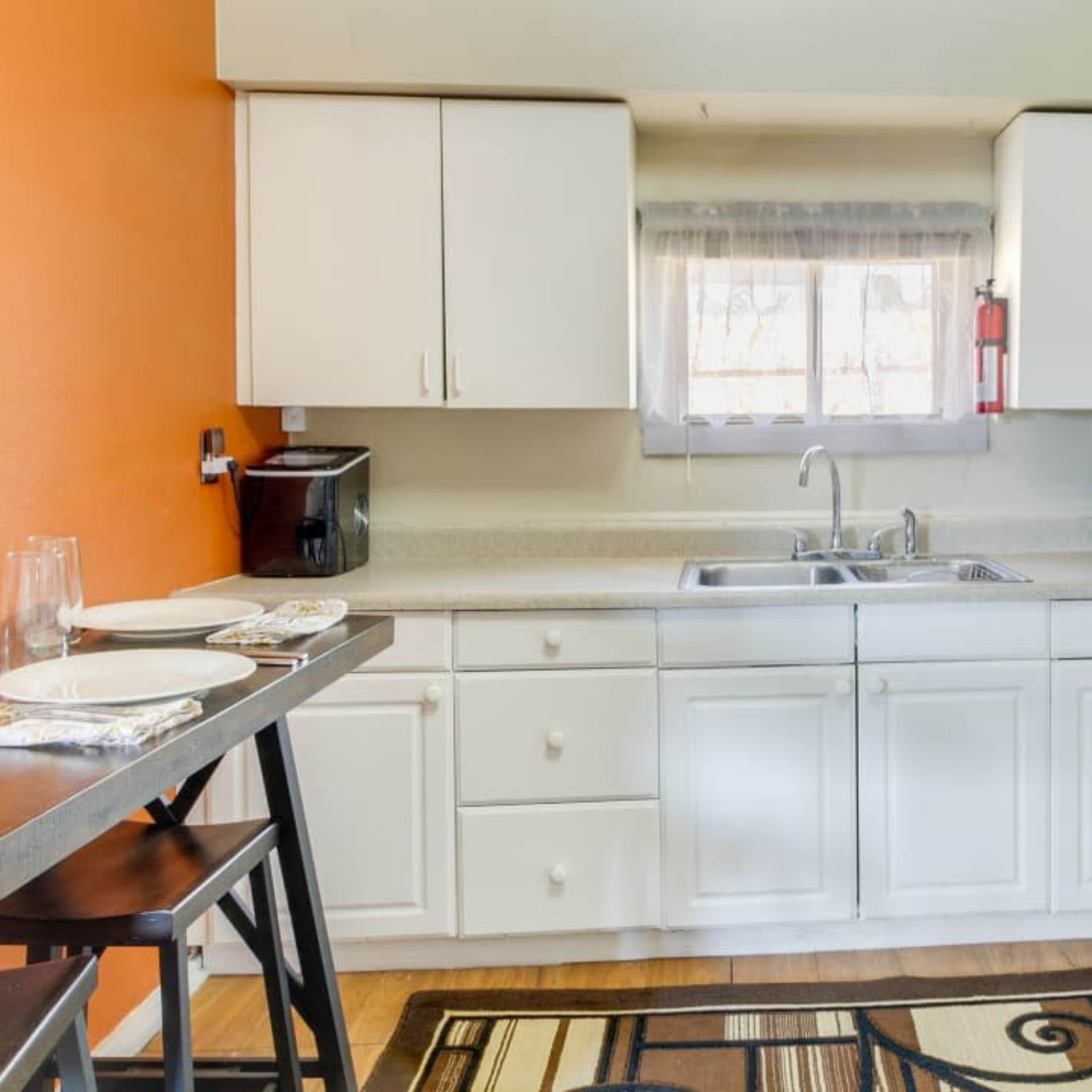 A kitchen features white cabinets, a stainless steel sink, a microwave, and a gas stove, with an orange wall and a window above the sink.