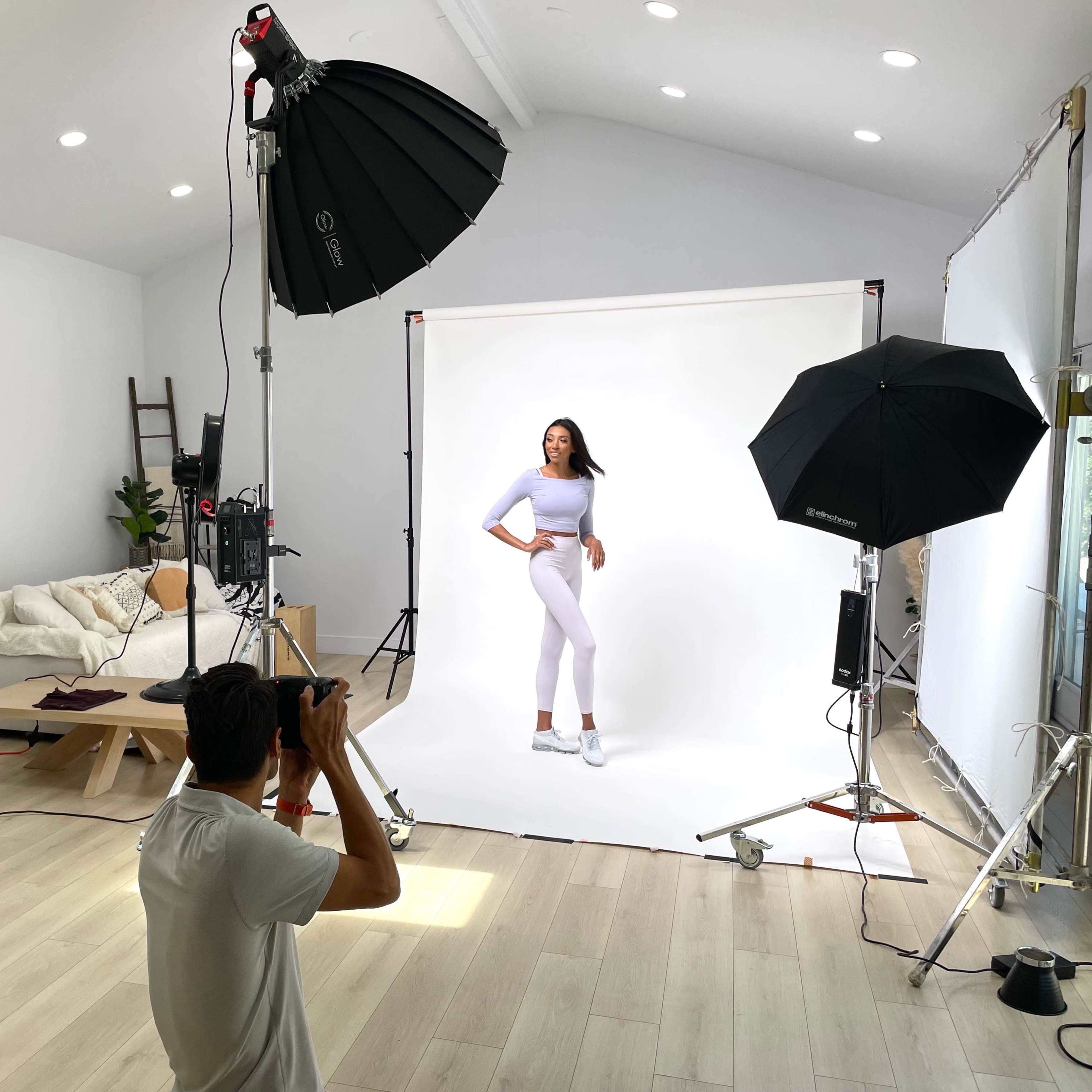 A model poses in a studio for a photoshoot while a photographer captures the moment.