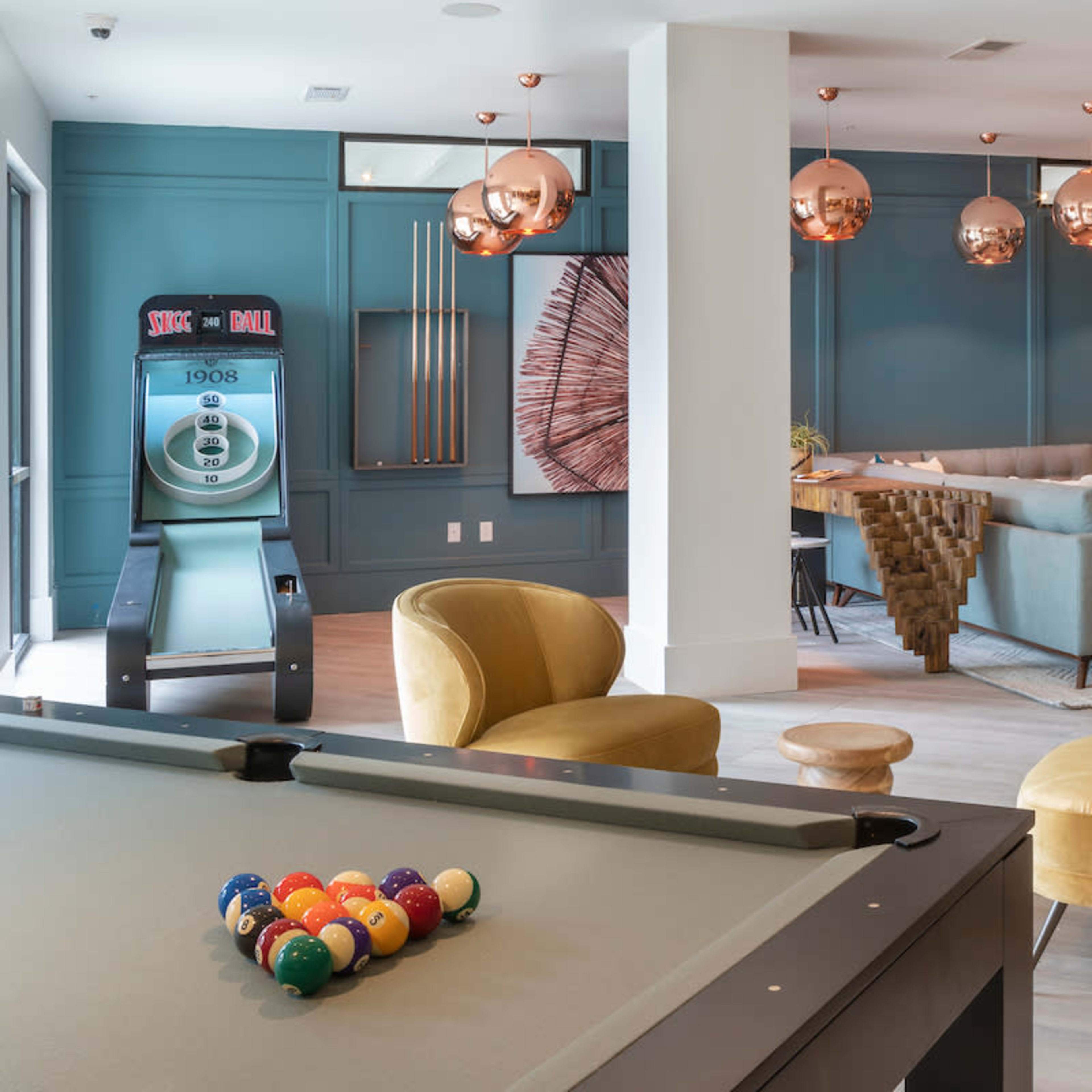 A modern lounge area with a pool table in the foreground and comfortable seating, including yellow chairs, in a stylishly decorated space.