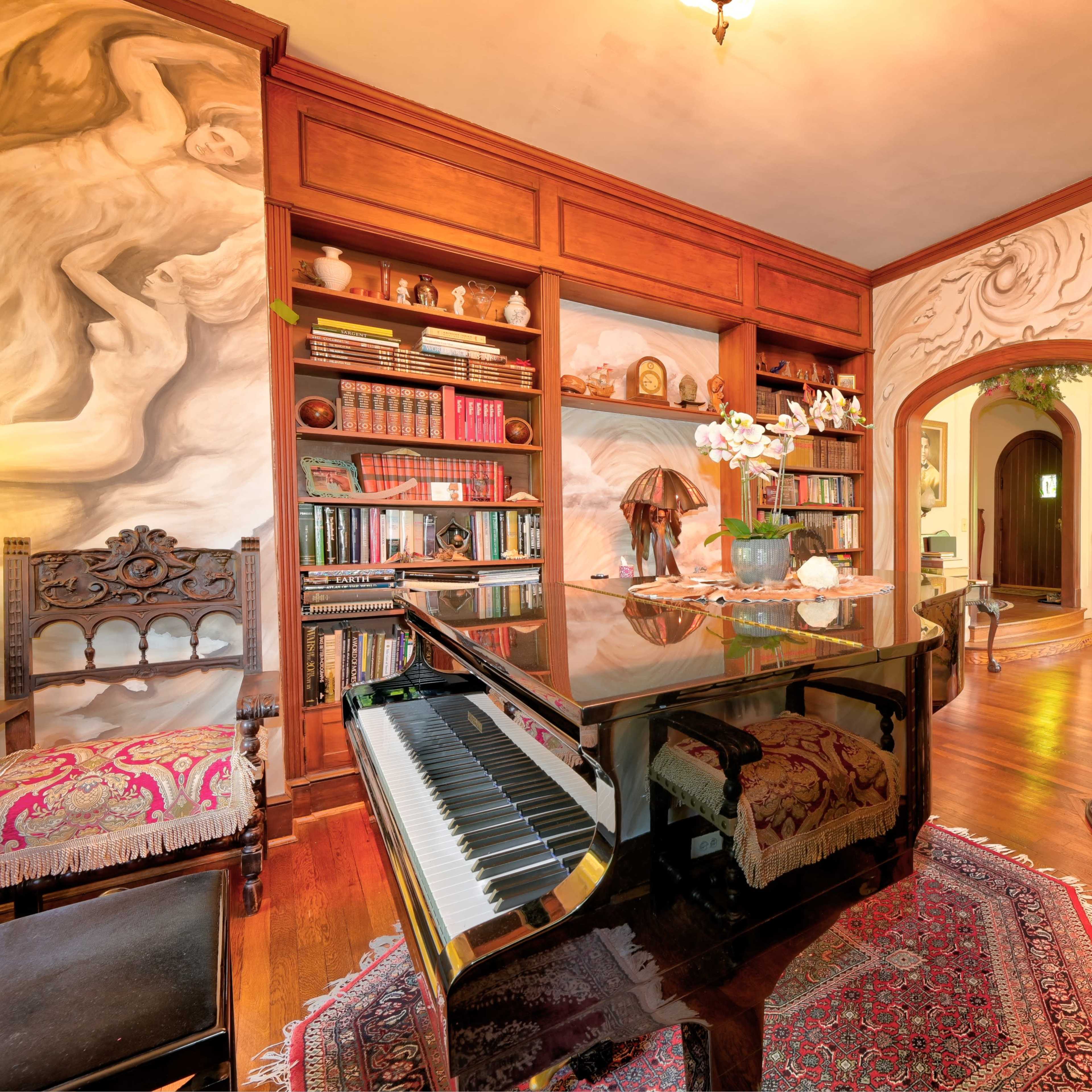 A grand piano sits in a room adorned with ornate wooden shelves filled with books, featuring a fireplace and detailed wall art.
