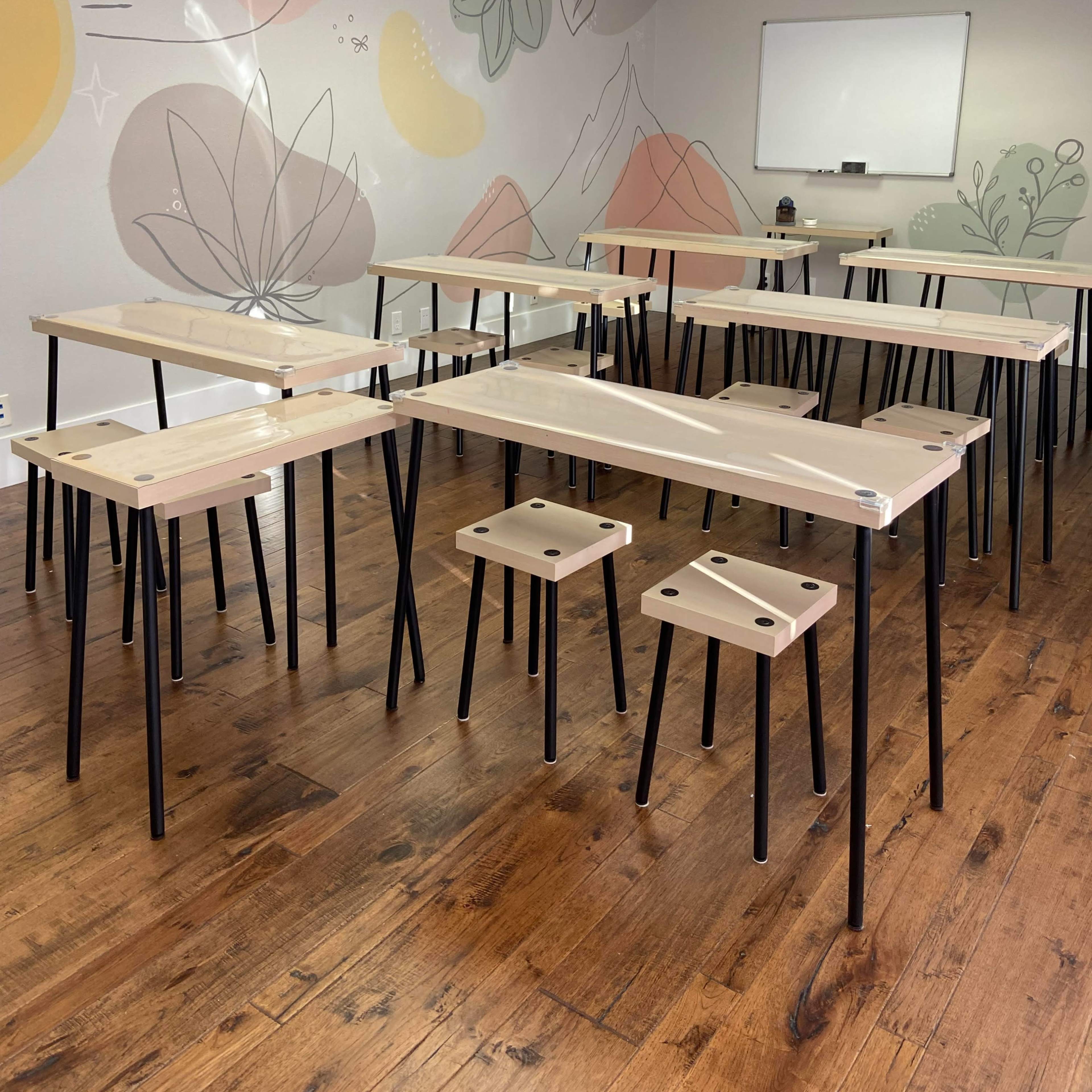 A group of wooden tables with black legs is arranged in a brightly lit room featuring a mural of plants and mountains on the wall.