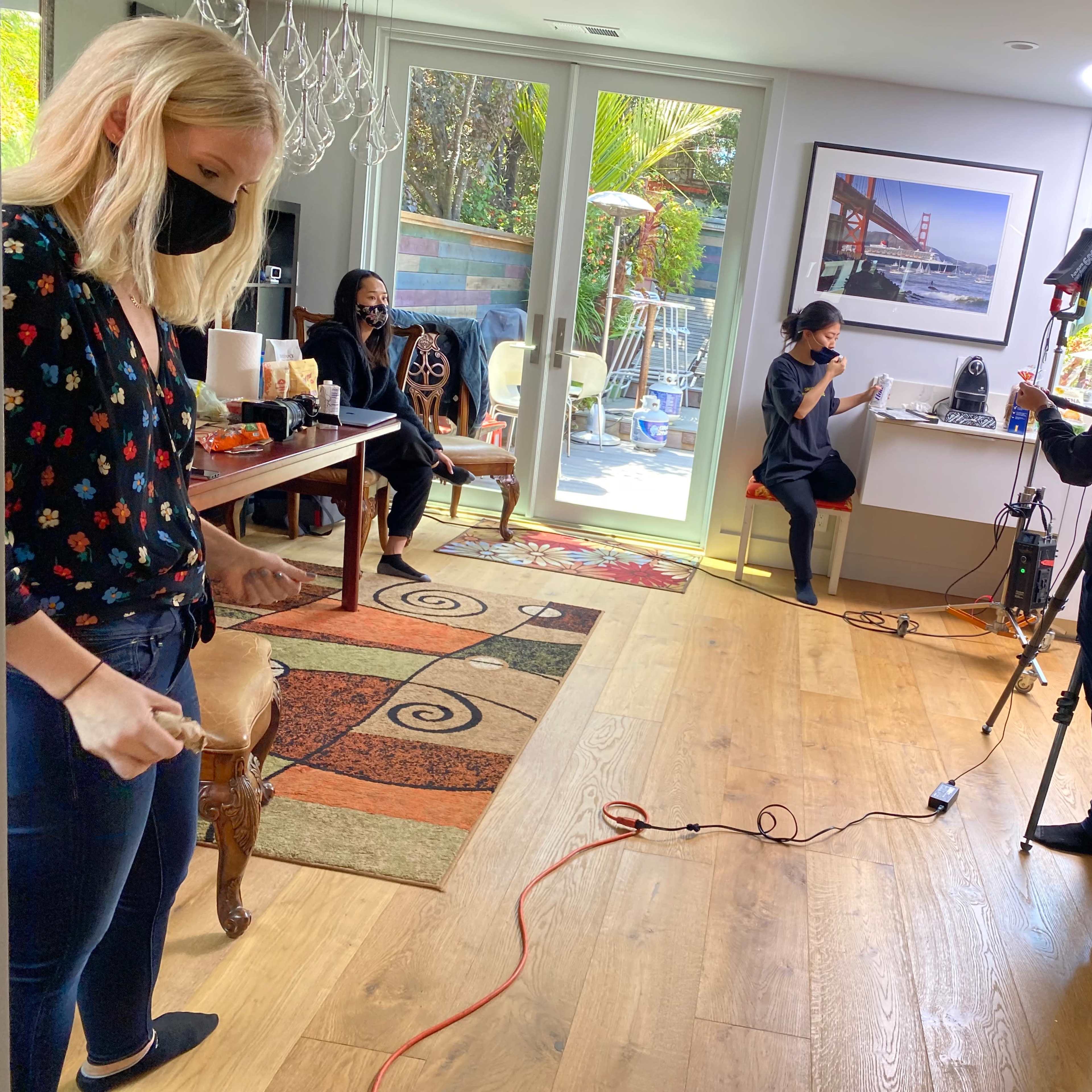 A group of people in a well-lit room preparing for a photoshoot, with a camera setup and lighting equipment in use.