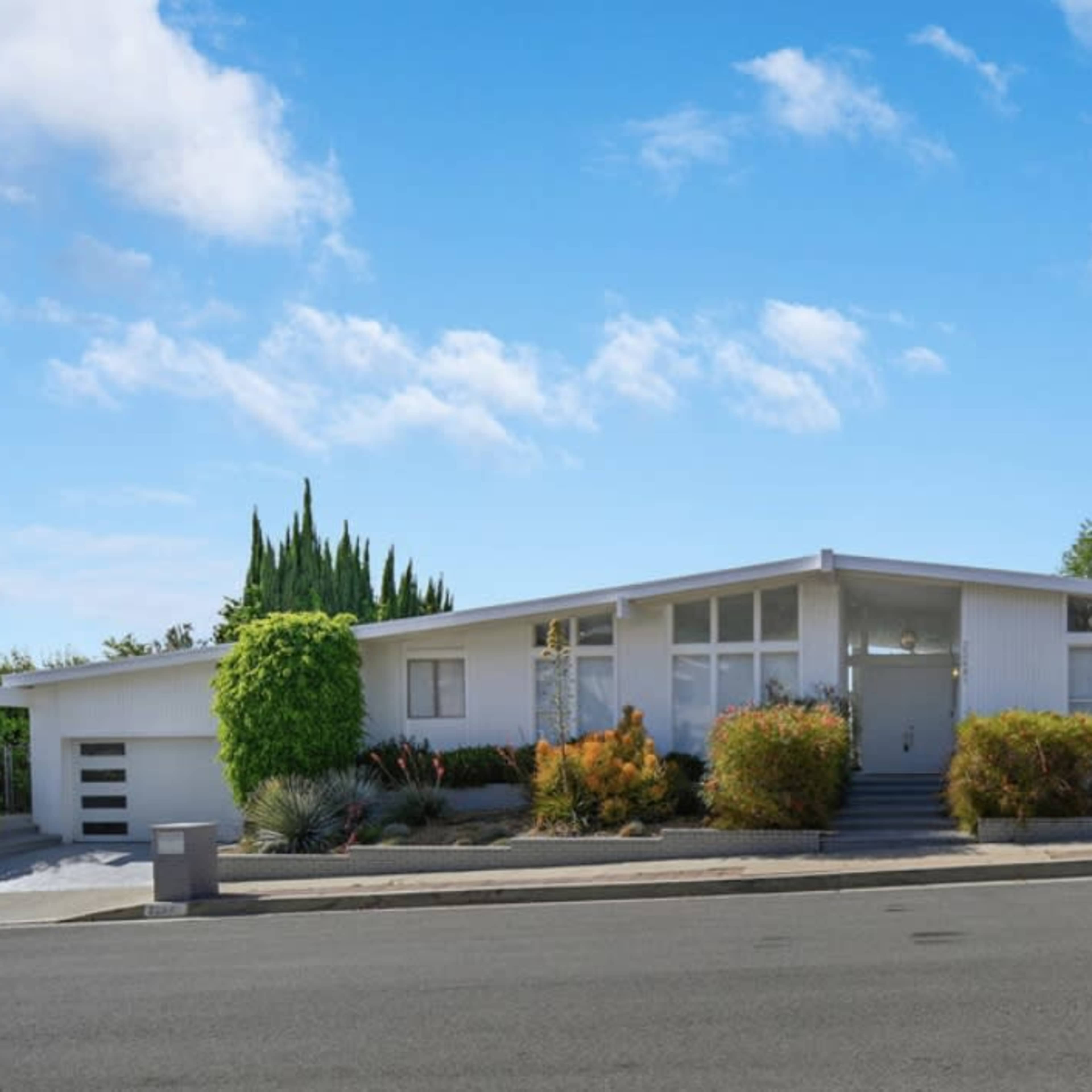 A modern white house with a landscaped front yard and a clear blue sky.