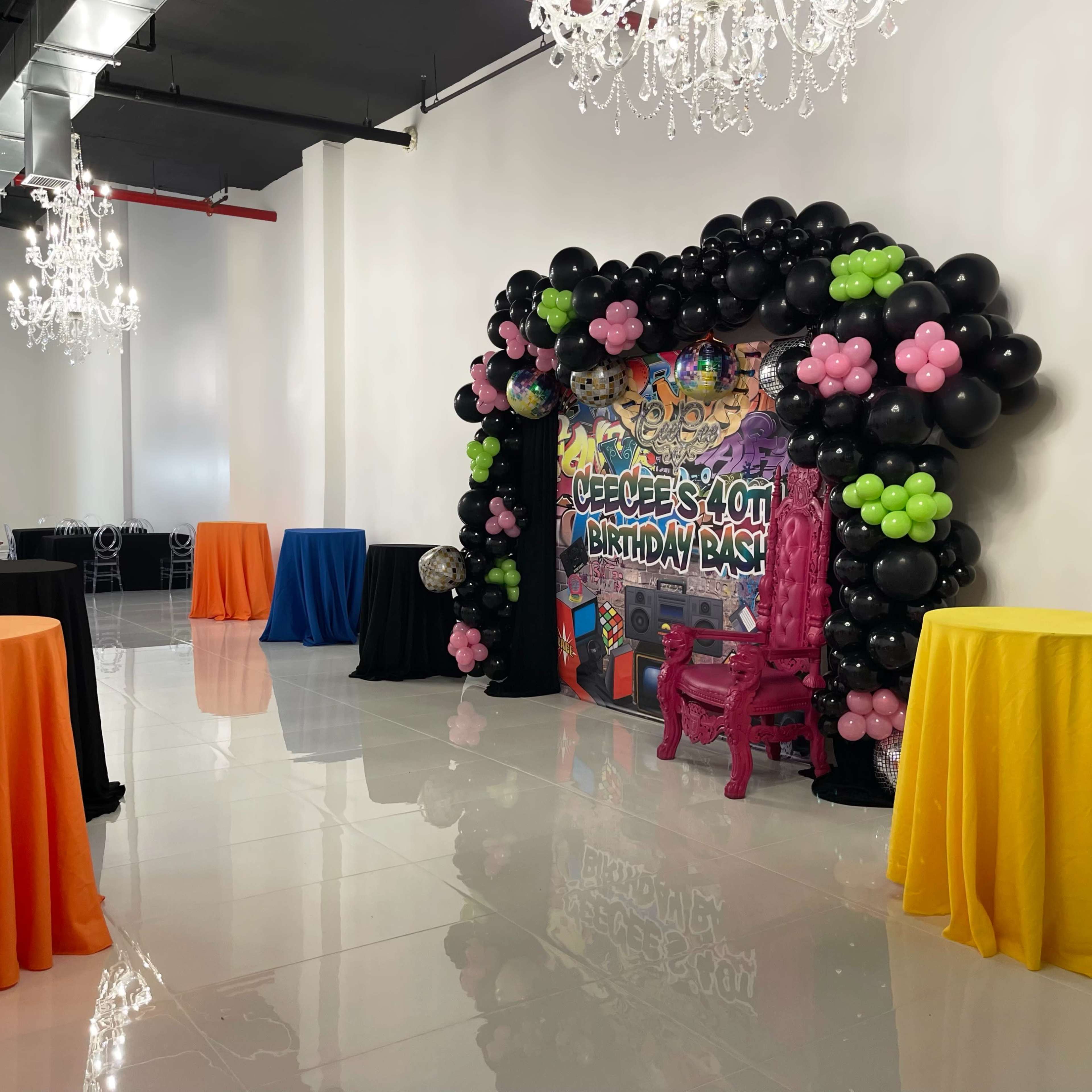 A brightly decorated event space featuring colorful tables and a large balloon arch with a birthday theme.
