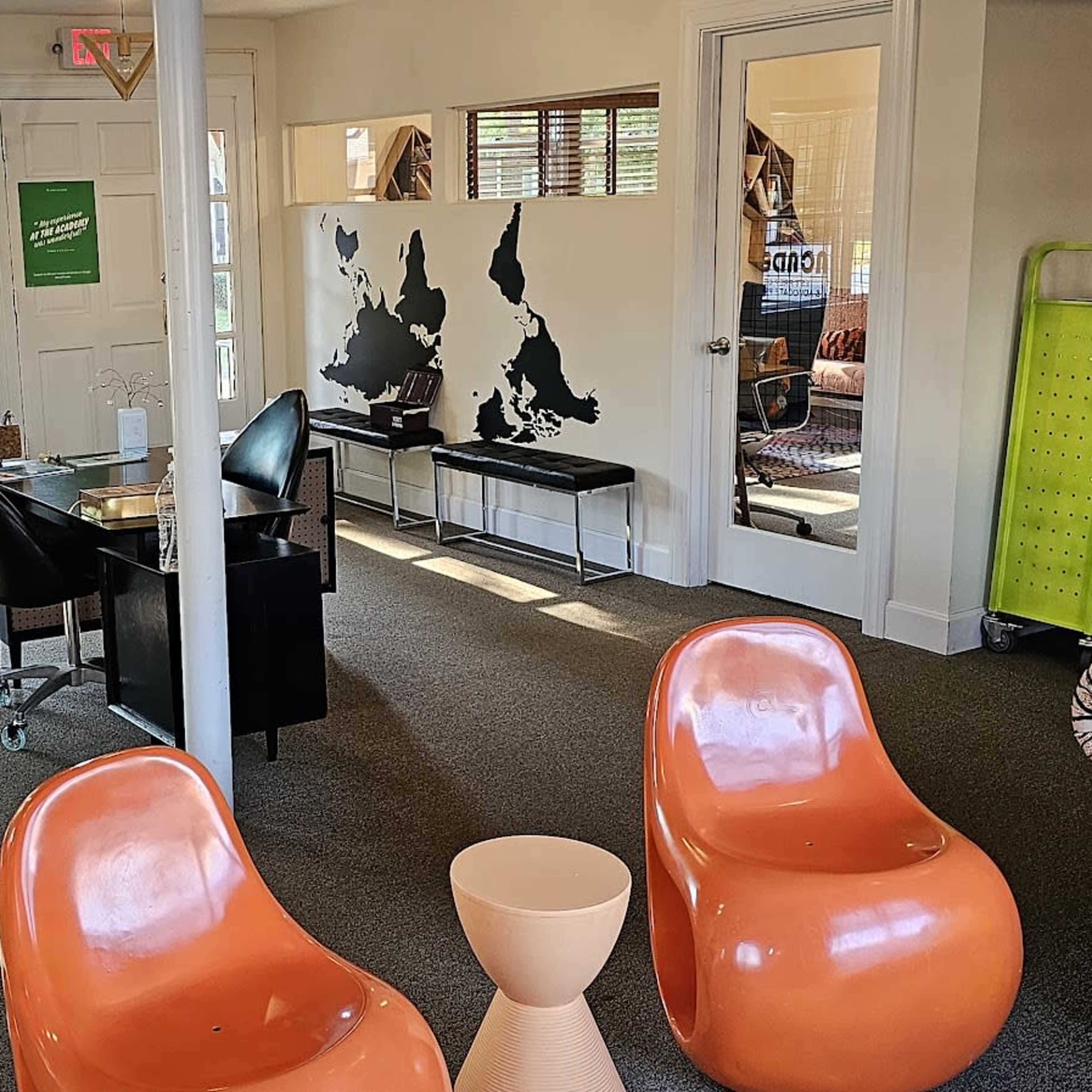 A modern office space with orange chairs, black furniture, and a large window allowing natural light to fill the room.