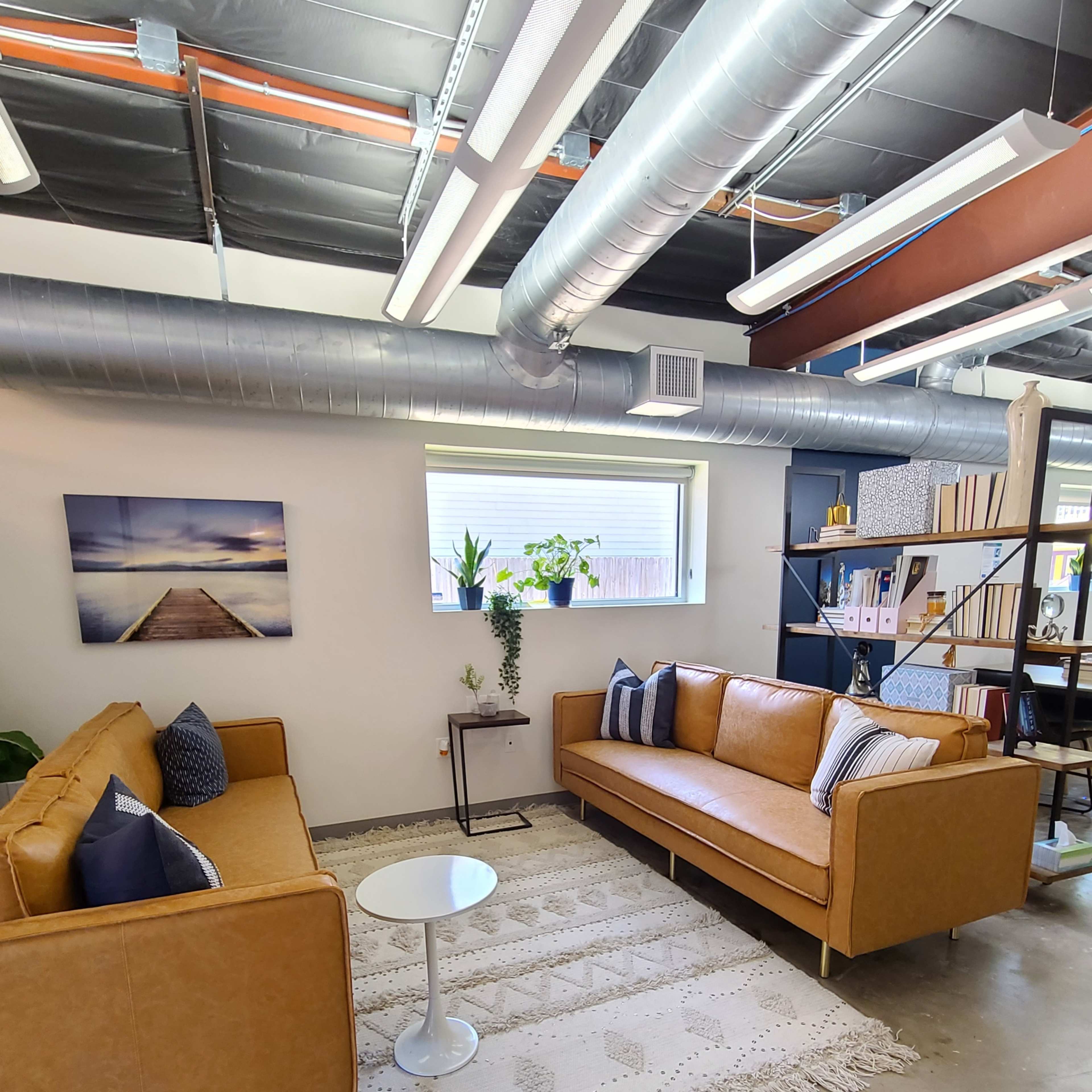 A modern office lounge area with two light brown sofas, a small white table, and a decorative rug placed on a concrete floor.