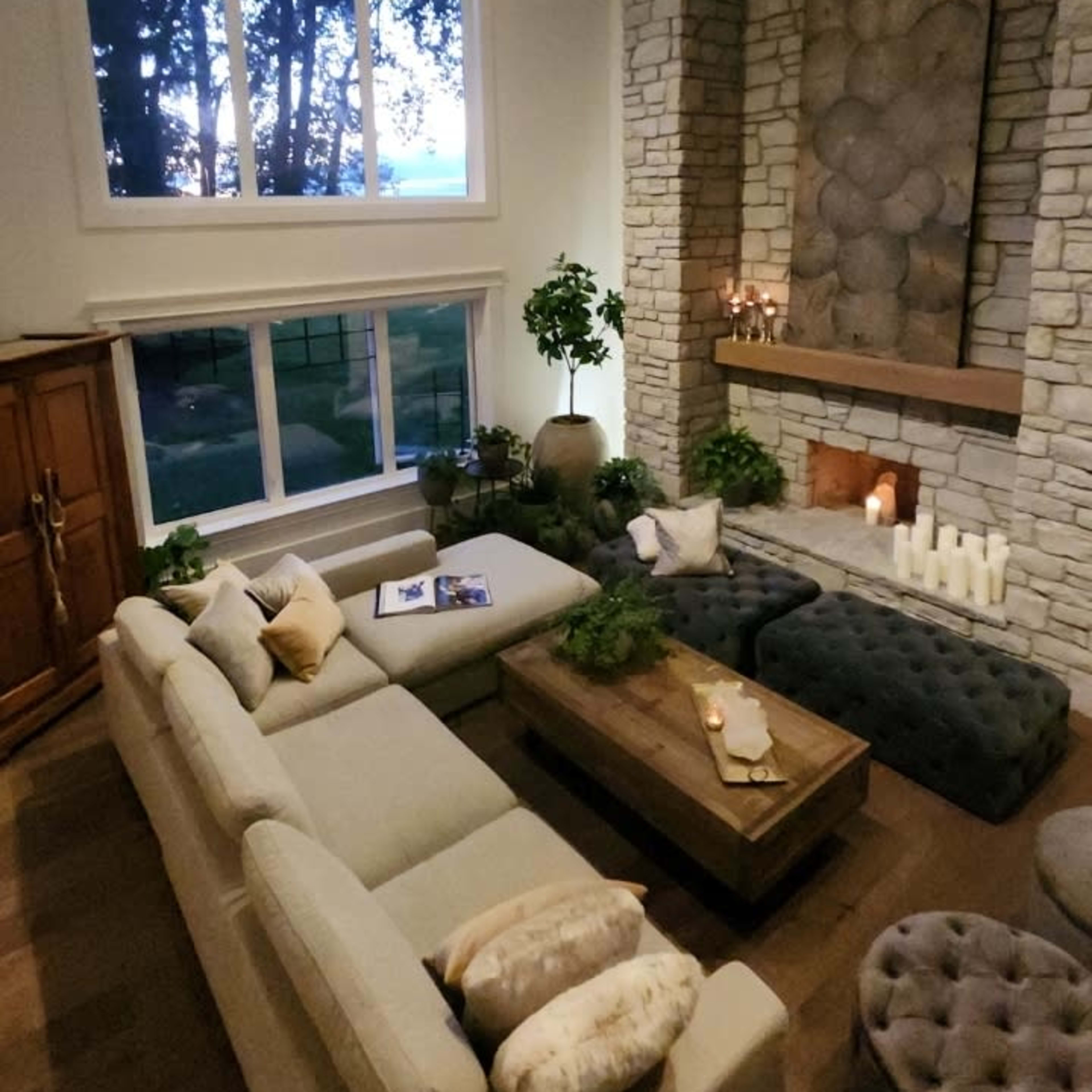 A spacious living room features a large sectional sofa, a stone fireplace, and large windows that provide a view of the outdoors.