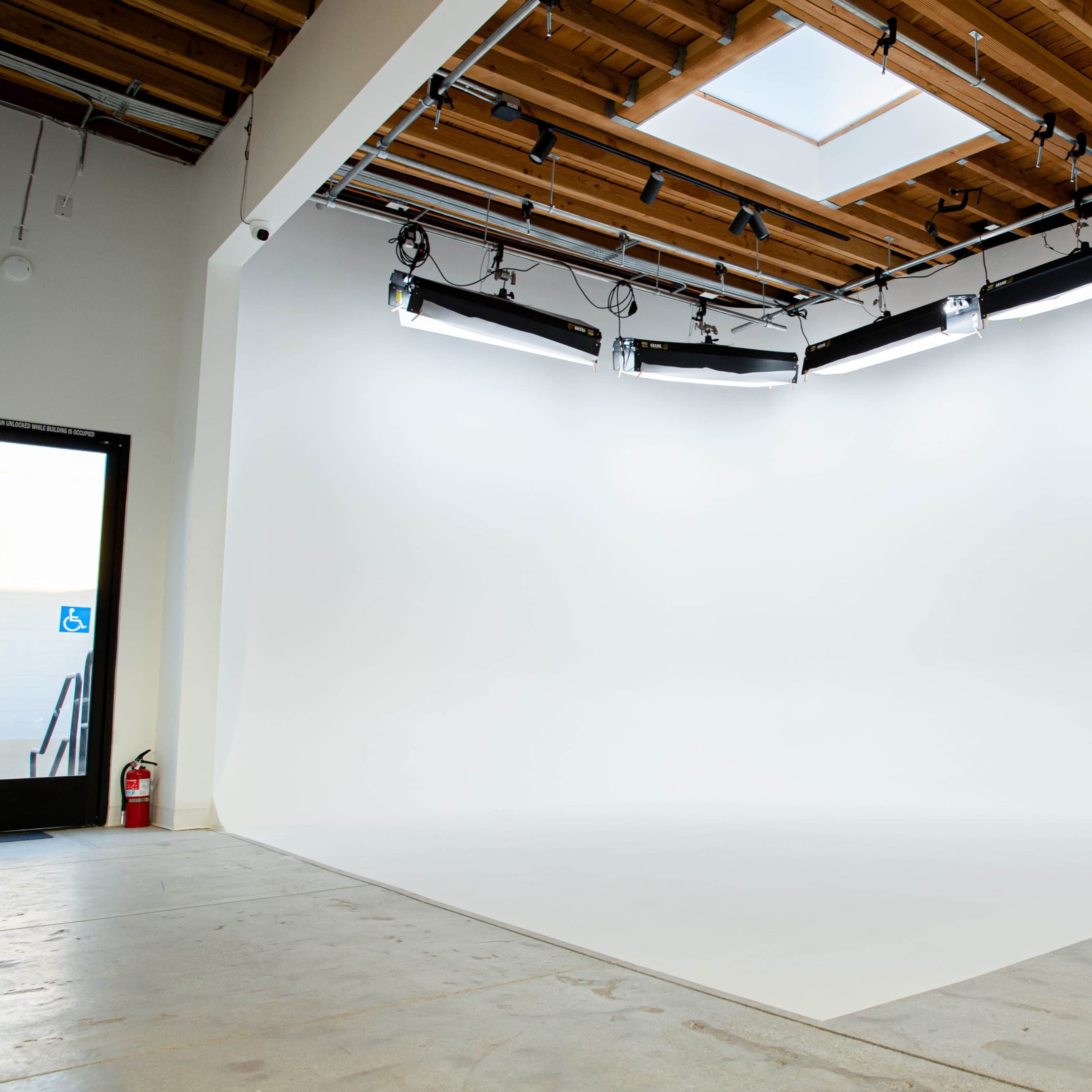 A spacious photography studio with a seamless white backdrop, overhead lighting, and a skylight.